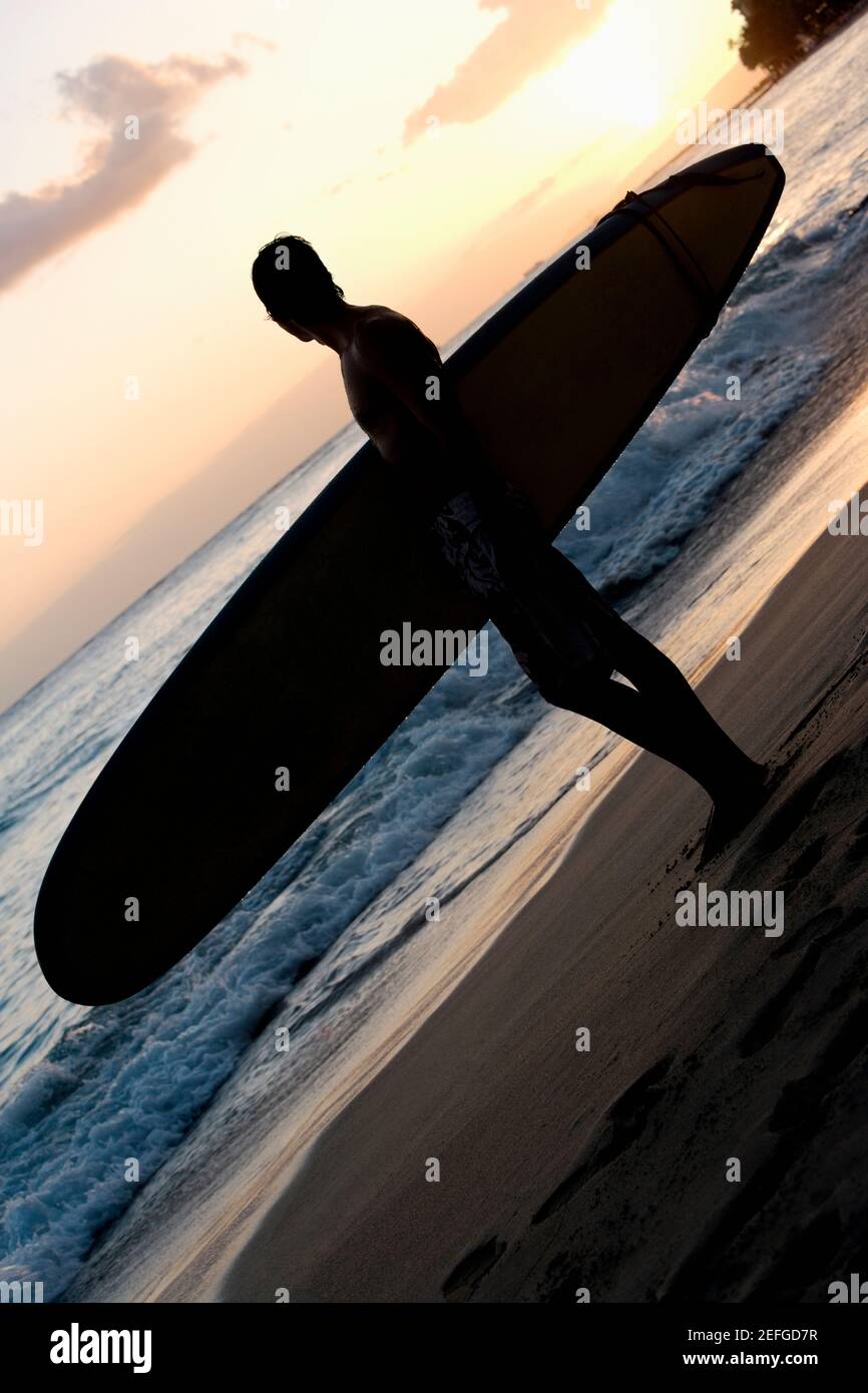 Silhouette d'un homme tenant une planche de surf et debout sur la plage, Waikiki Beach, Honolulu, Oahu, îles Hawaii, ÉTATS-UNIS Banque D'Images