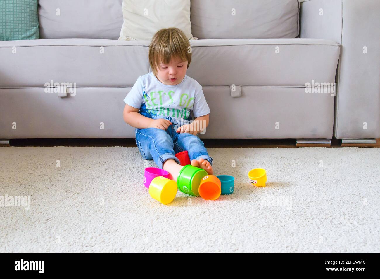 enfant solitaire avec le syndrome de down jouant dans la salle de séjour avec ses jouets pendant la quarantaine de covid Banque D'Images