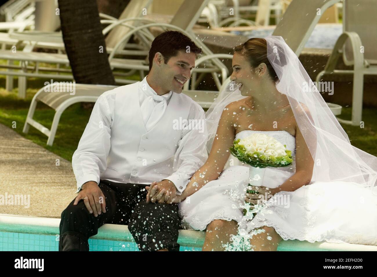 Couple nouvellement mariés assis au bord de la piscine et souriant Banque D'Images