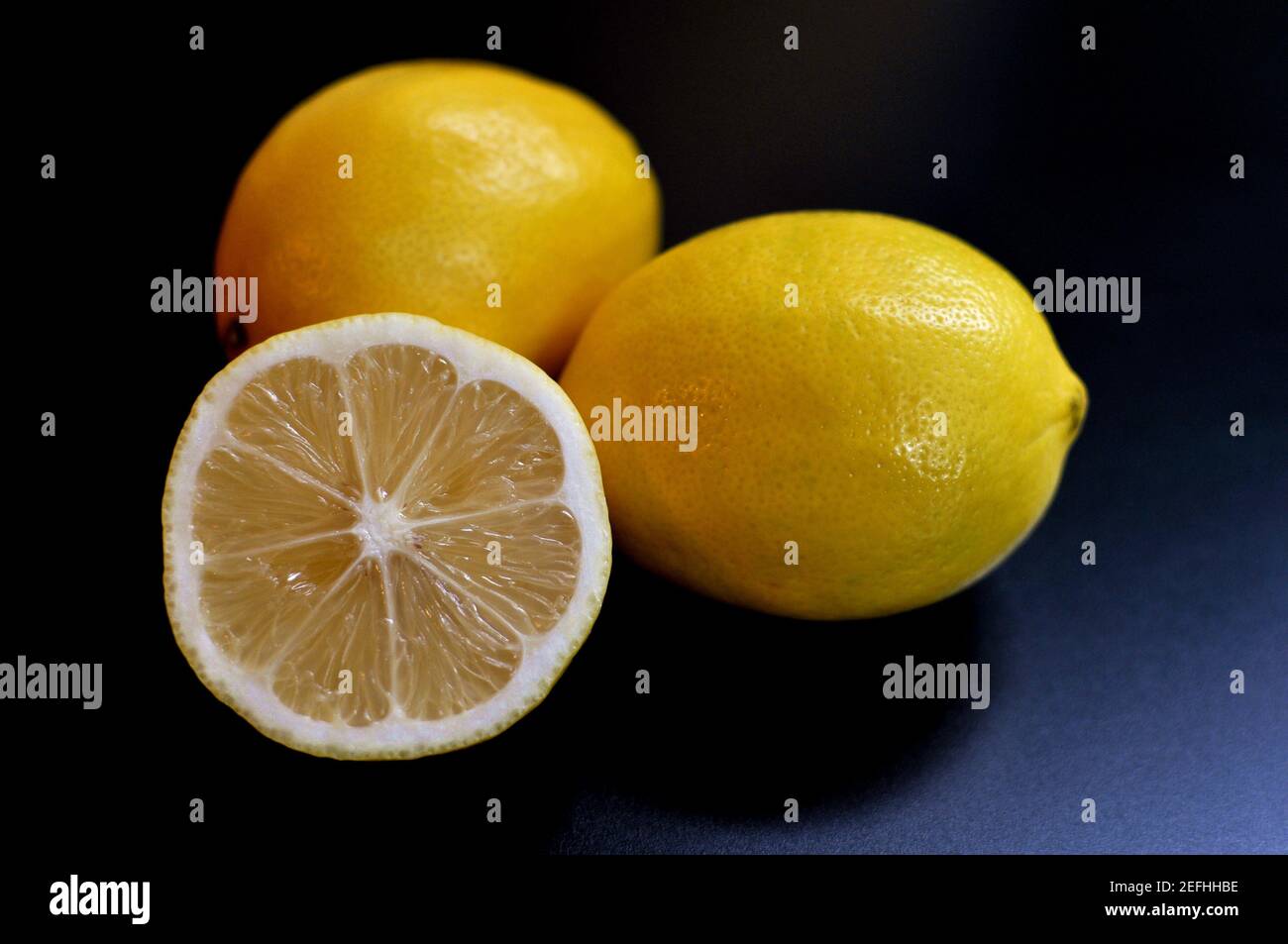 3 citrons, deux entiers et un demi sur fond noir. Sous-exposé intentionnel Banque D'Images