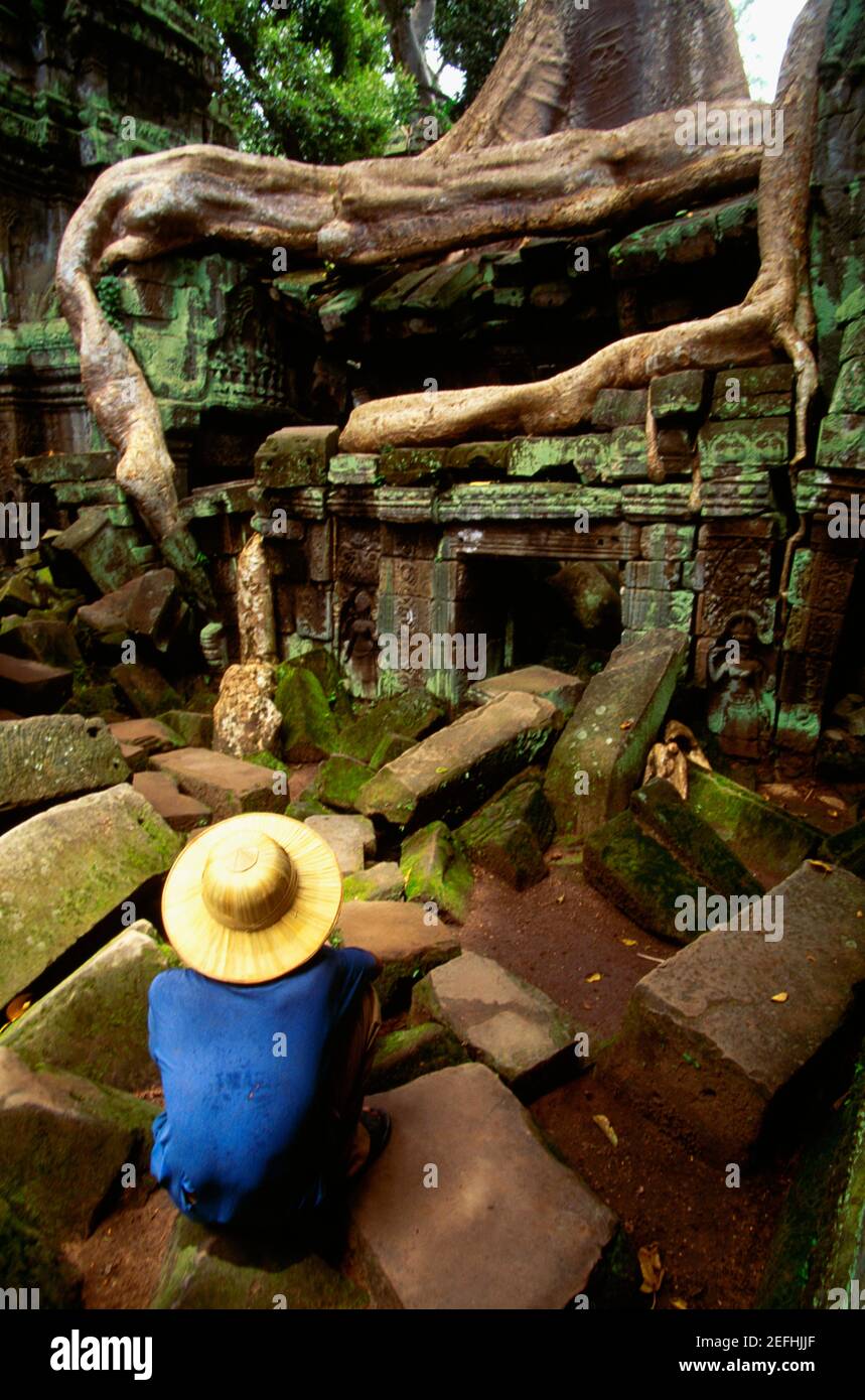 Vue à grand angle d'un homme qui se croupe sur une pierre en face d'un temple, Temple Ta Prohm, Angkor, Siem Reap, Cambodge Banque D'Images