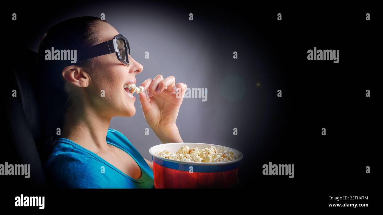 Une jeune femme au cinéma regarde un film en lunettes 3D et avec du pop-corn dans ses mains. Banque D'Images