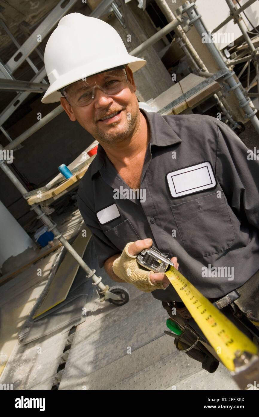 Portrait d'un ouvrier de la construction de sexe masculin tenant une mesure à ruban et souriant Banque D'Images