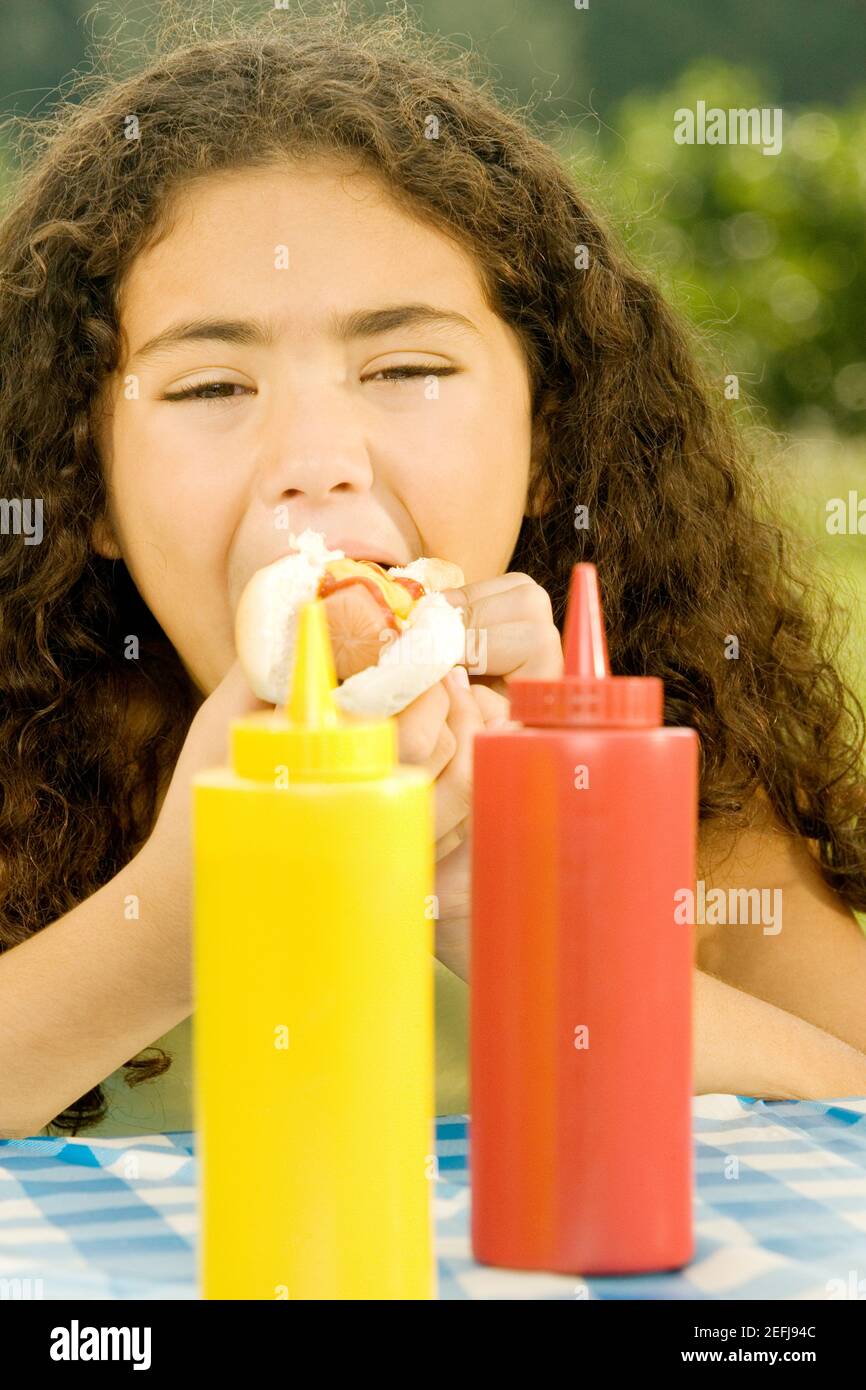 Gros plan d'une fille mangeant un hamburger derrière des bouteilles de sauce Banque D'Images
