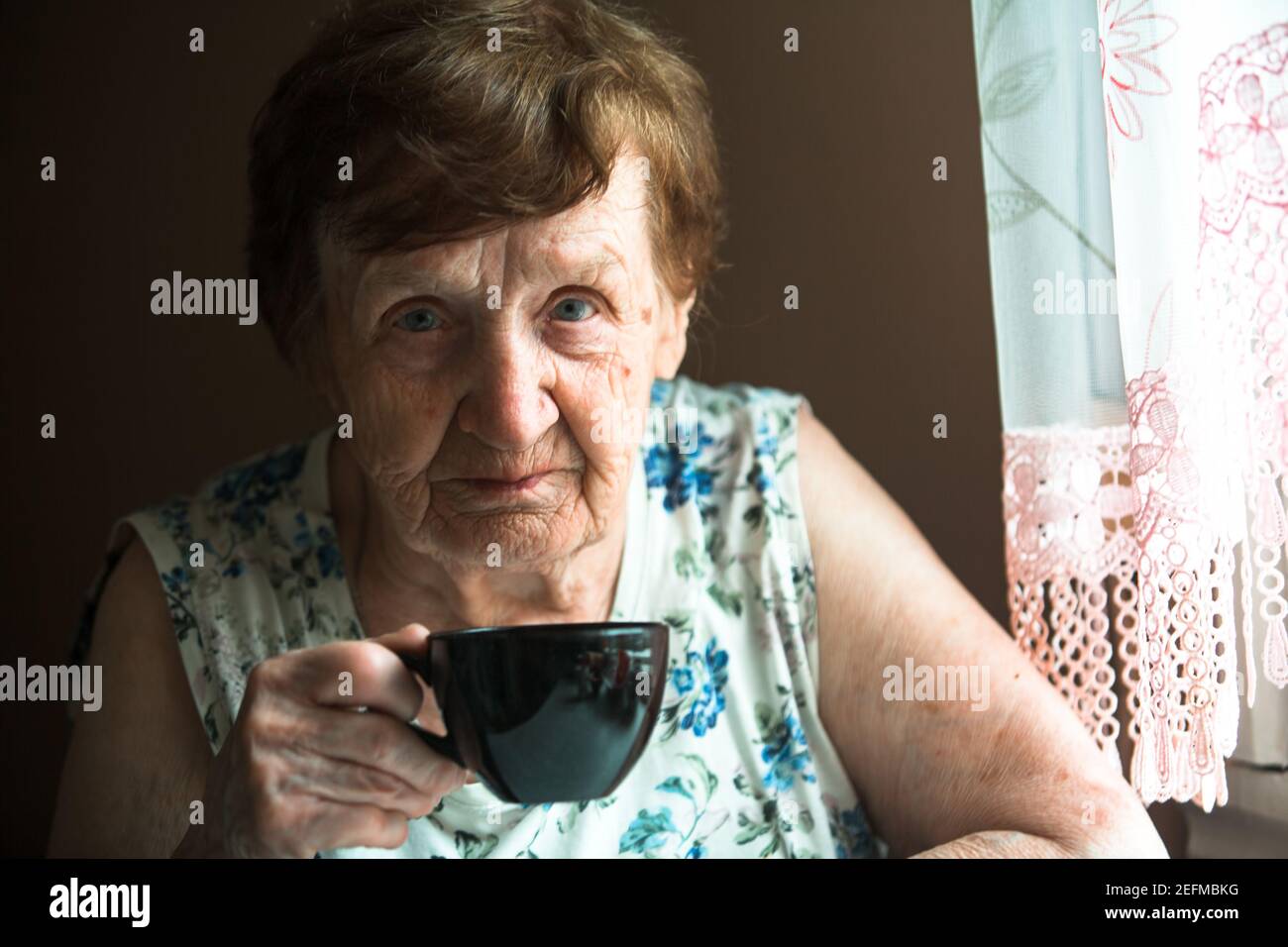 Portrait d'une vieille femme qui boit du thé à la maison. Banque D'Images