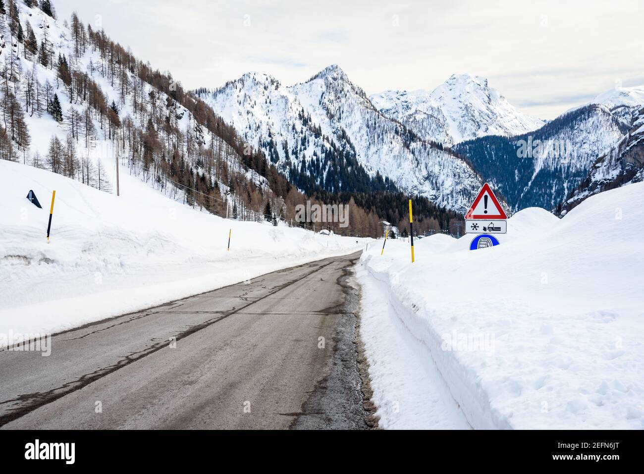 Panneau d'avertissement dans la neige profonde le long d'une montagne vide Route dans les Alpes européennes par une journée d'hiver nuageux Banque D'Images