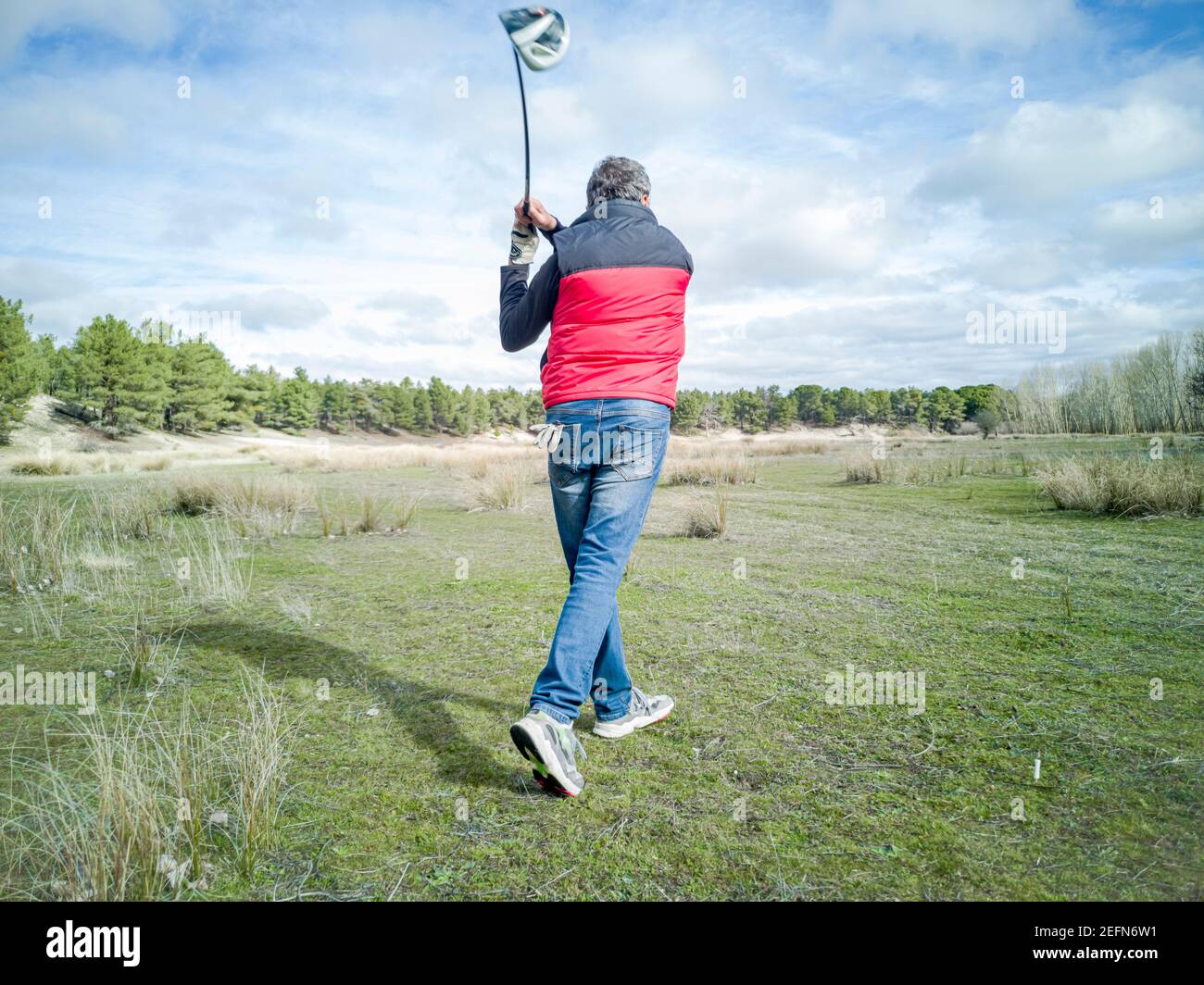 Senior citoyen pratiquant son swing de golf sur un terrain rustique par temps nuageux Banque D'Images