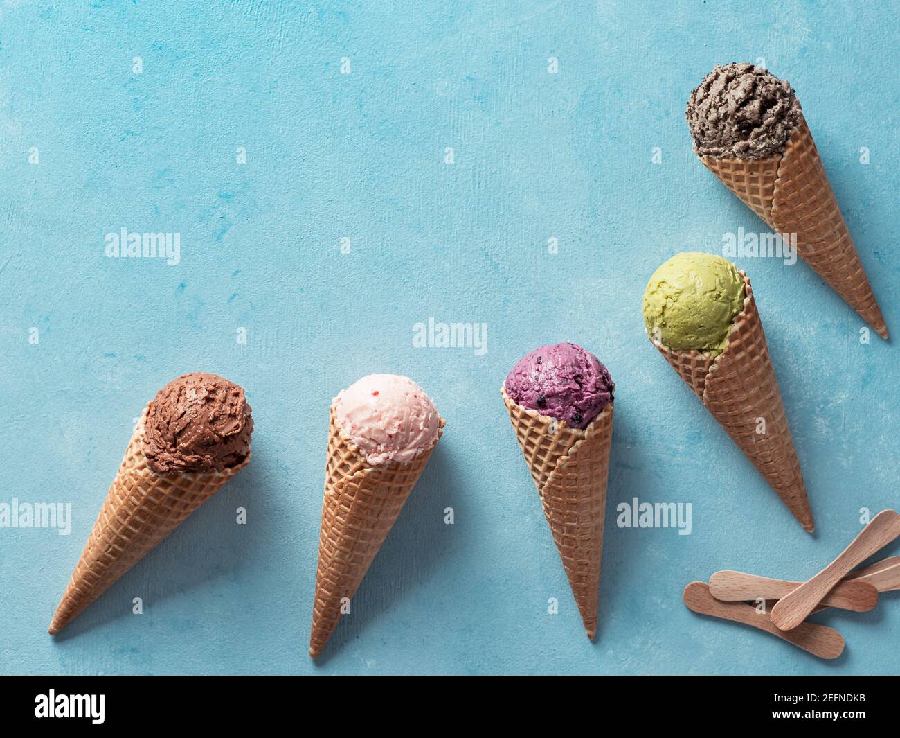 Diverses boules de glace dans des cônes avec copie espace. La crème glacée dans des cônes de couleur chocolat, fraise, myrtille, pistache ou chocolat, biscuits matcha cookies sandwich sur fond bleu. Vue d'en haut Banque D'Images