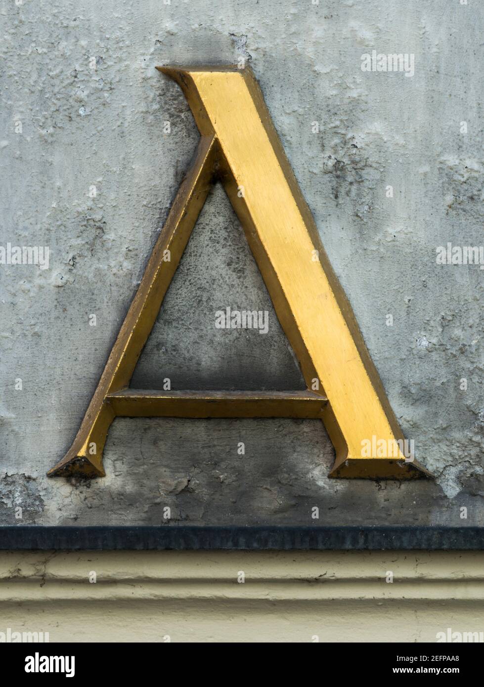 Lettre d'or A avec serifs sur un mur gris Banque D'Images