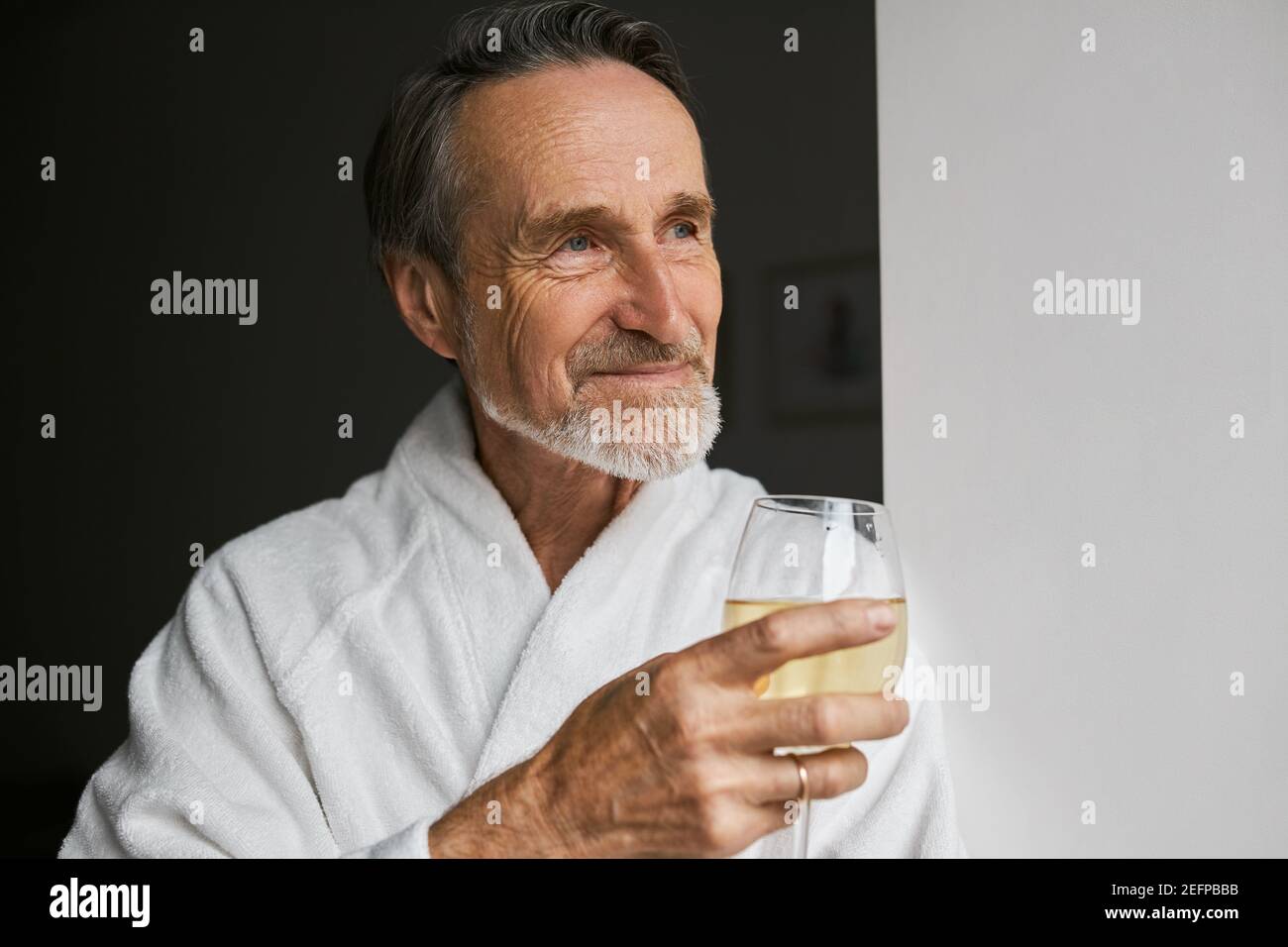 Gros plan d'un homme mûr souriant portant un peignoir blanc wineglass Banque D'Images