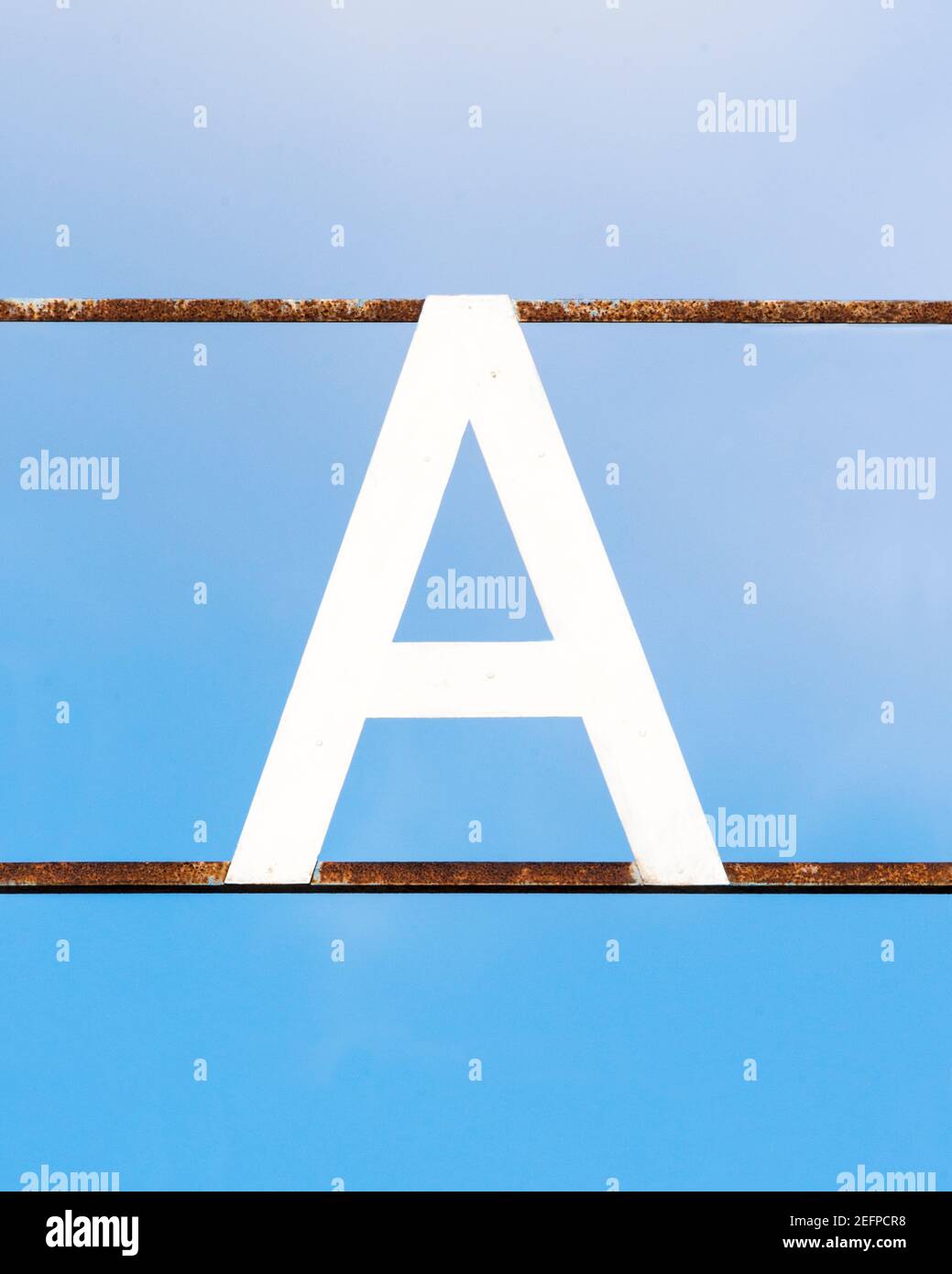 Lettre blanche A attachée aux barres métalliques rouillées contre A. ciel bleu Banque D'Images
