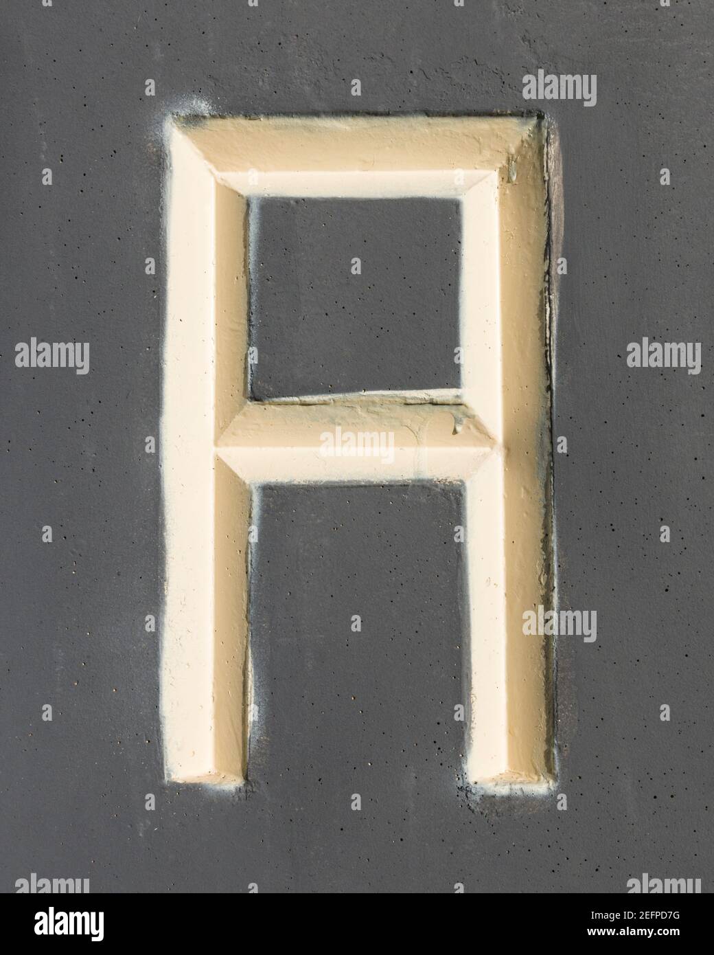 Lettre beige RELIEF négatif en béton peint gris Banque D'Images