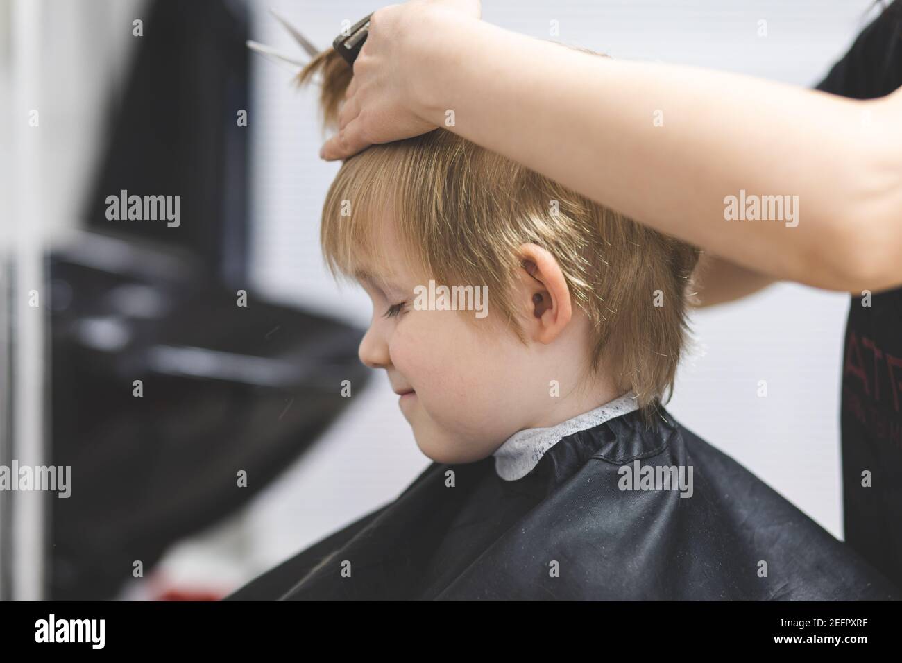 Le coiffeur coupe les cheveux heureux sourire blond enfant garçon. Gros plan sur le style de vie. Concept de beauté, d'hygiène. Banque D'Images