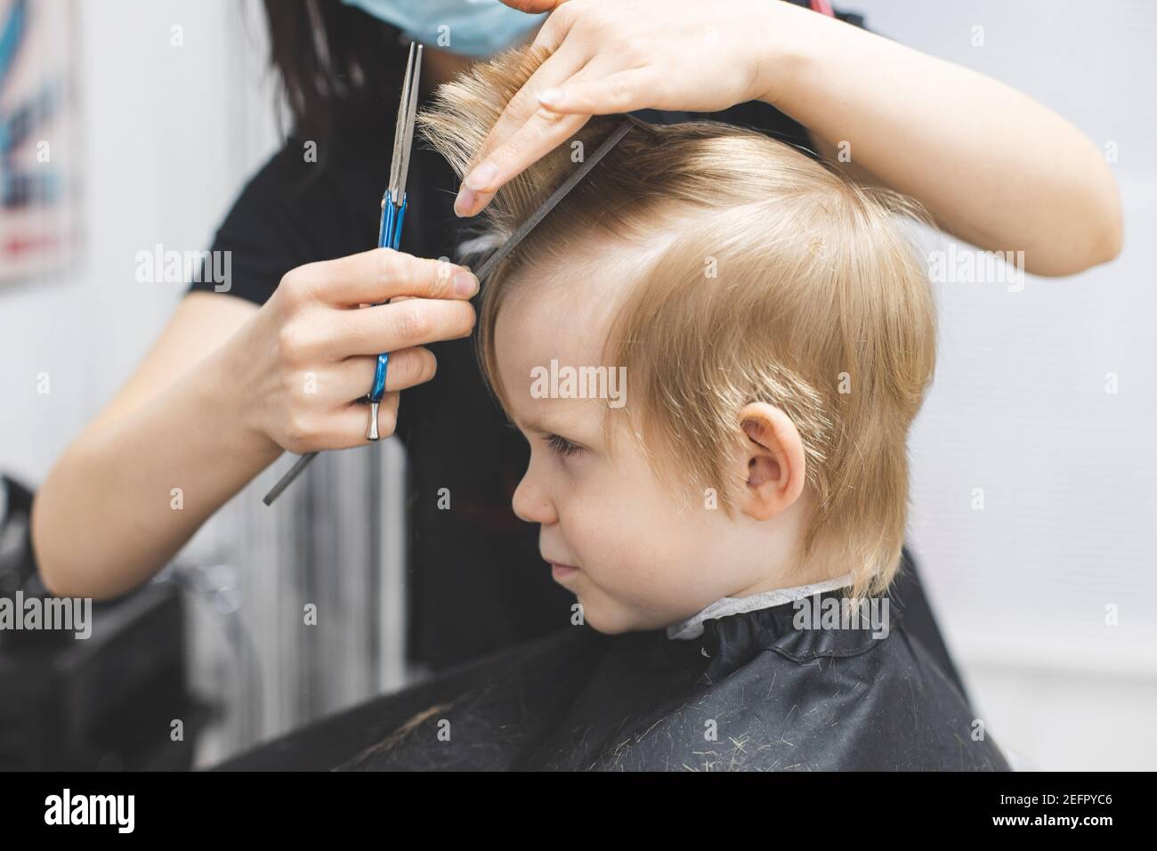 Le coiffeur coupe les cheveux sérieux blond strict enfant garçon. Gros plan sur le style de vie. Concept de beauté, d'hygiène. Banque D'Images