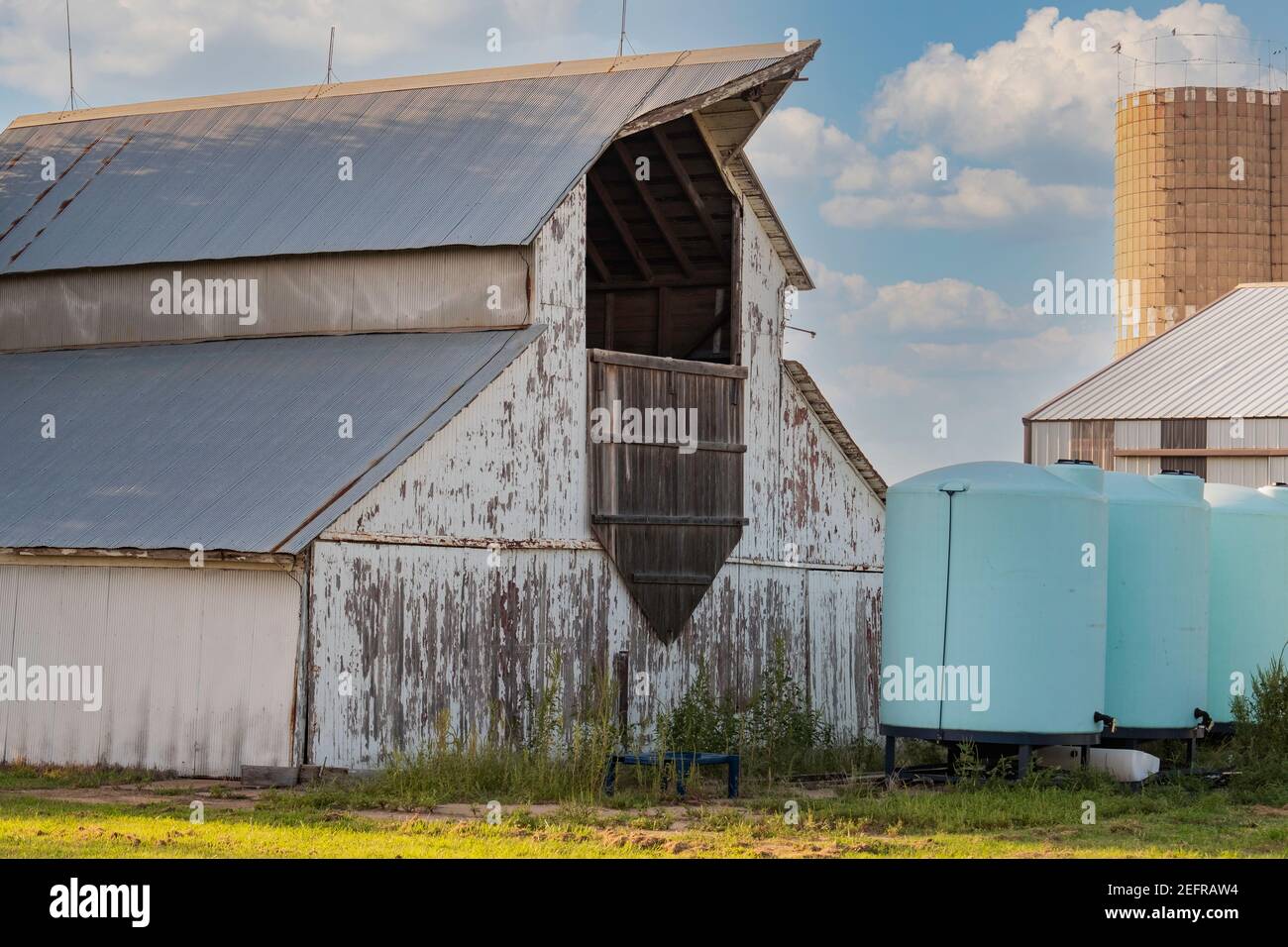 Grange américaine avec peinture blanche à écailler et toit en étain. Des réservoirs de stockage, un silo et une sortie dans une cour de ferme. ÉTATS-UNIS. Banque D'Images