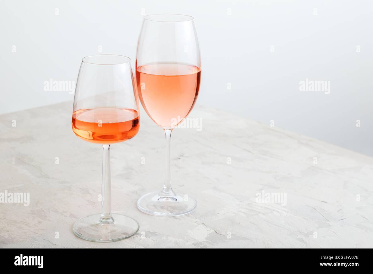 Vin de rose dans différents types de verres sur fond de béton léger. Composition minimale de vin sur table blanche avec espace de copie Banque D'Images