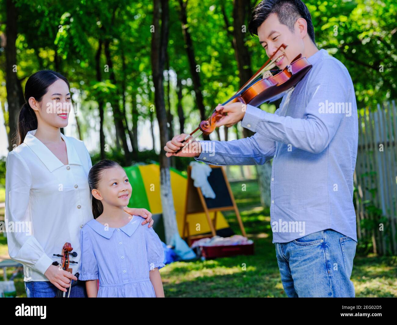 Un homme jouant du violon dans le parc avec sa femme et fille Banque D'Images