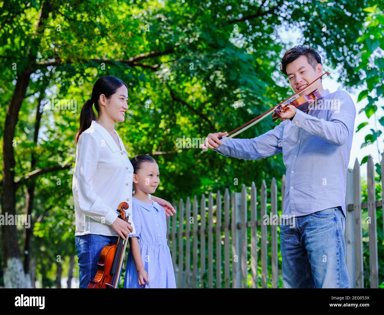 Un homme jouant du violon dans le parc avec sa femme et fille Banque D'Images