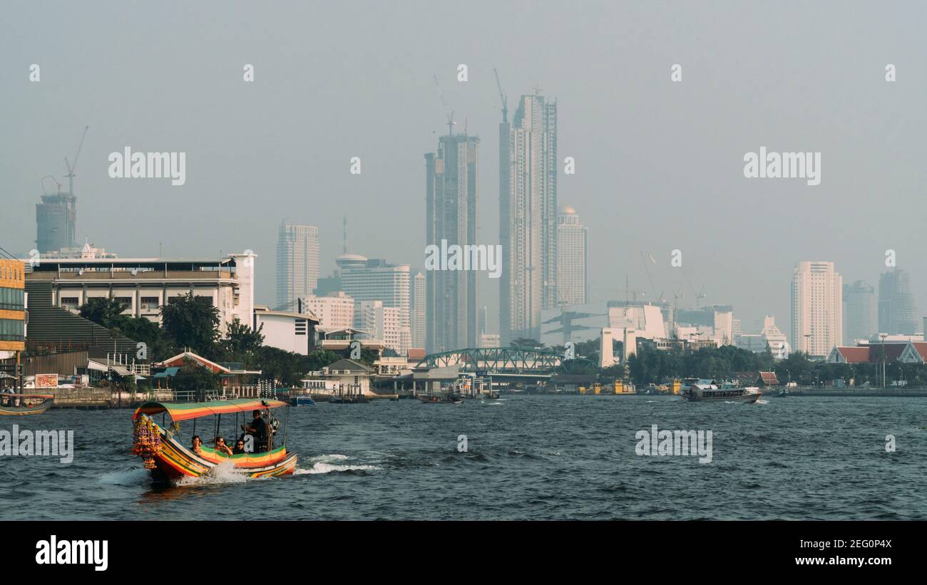 Air gris pollué du centre-ville de Bangkok depuis la rivière Chao Praya, avec bateau coloré passant par. Banque D'Images