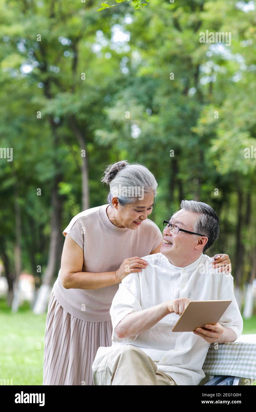 Les couples de personnes âgées heureux utilisent des tablettes électroniques dans le parc Banque D'Images