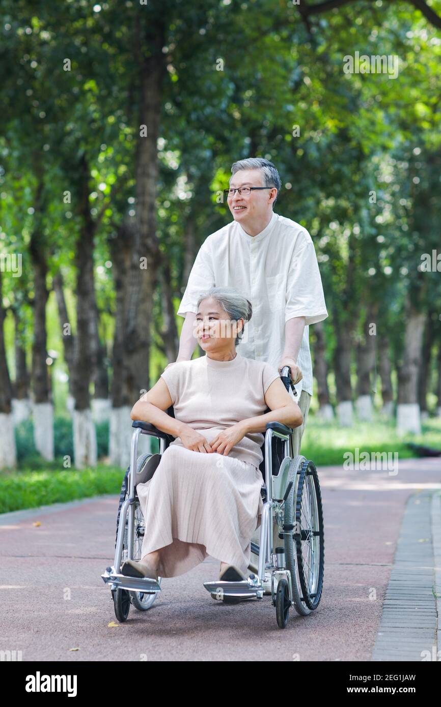 Le vieil homme pousse sa femme dans un fauteuil roulant le parc Banque D'Images