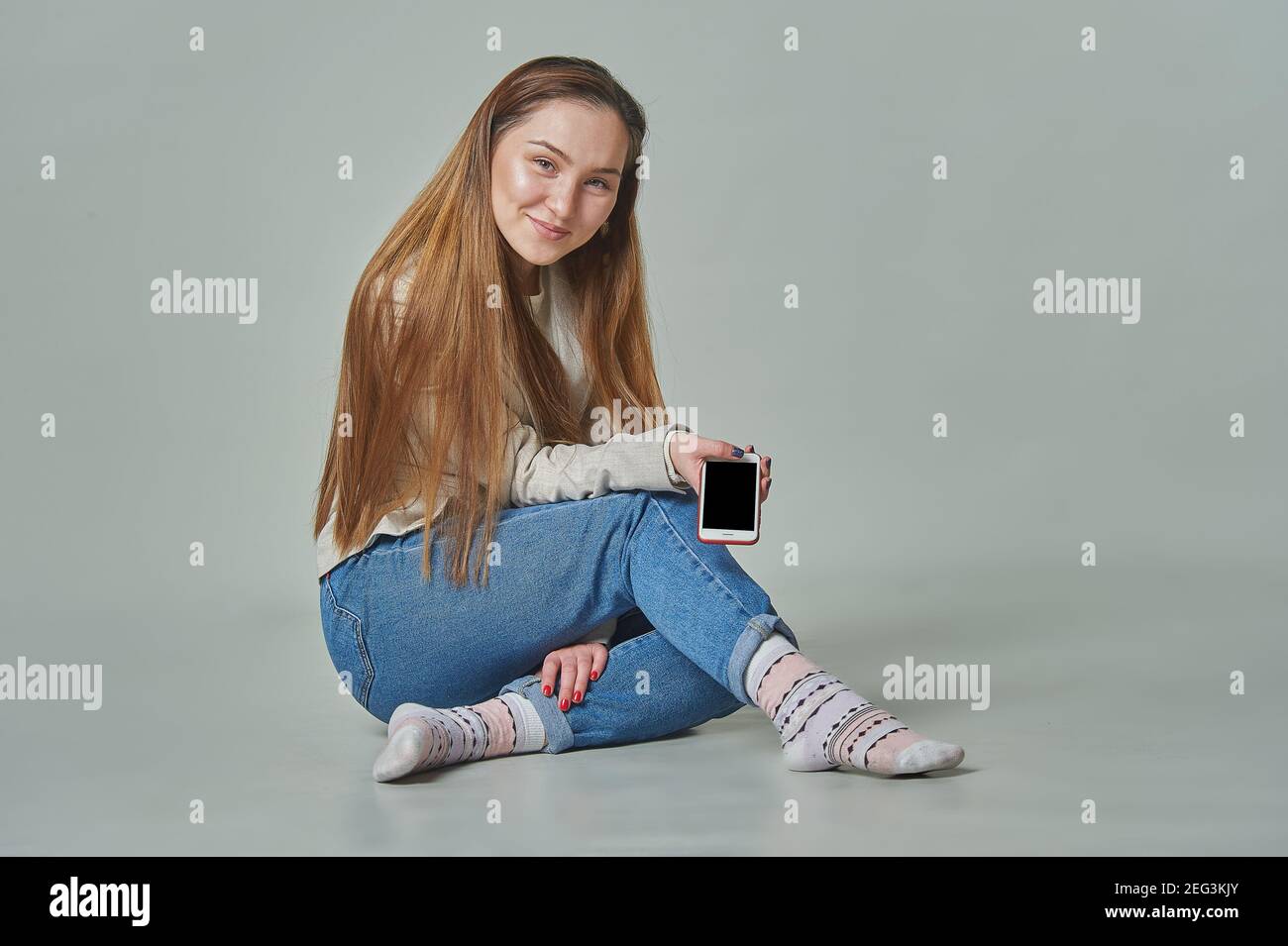 Une fille s'assoit à l'arrière-plan avec un téléphone ses mains et ses sourires Banque D'Images