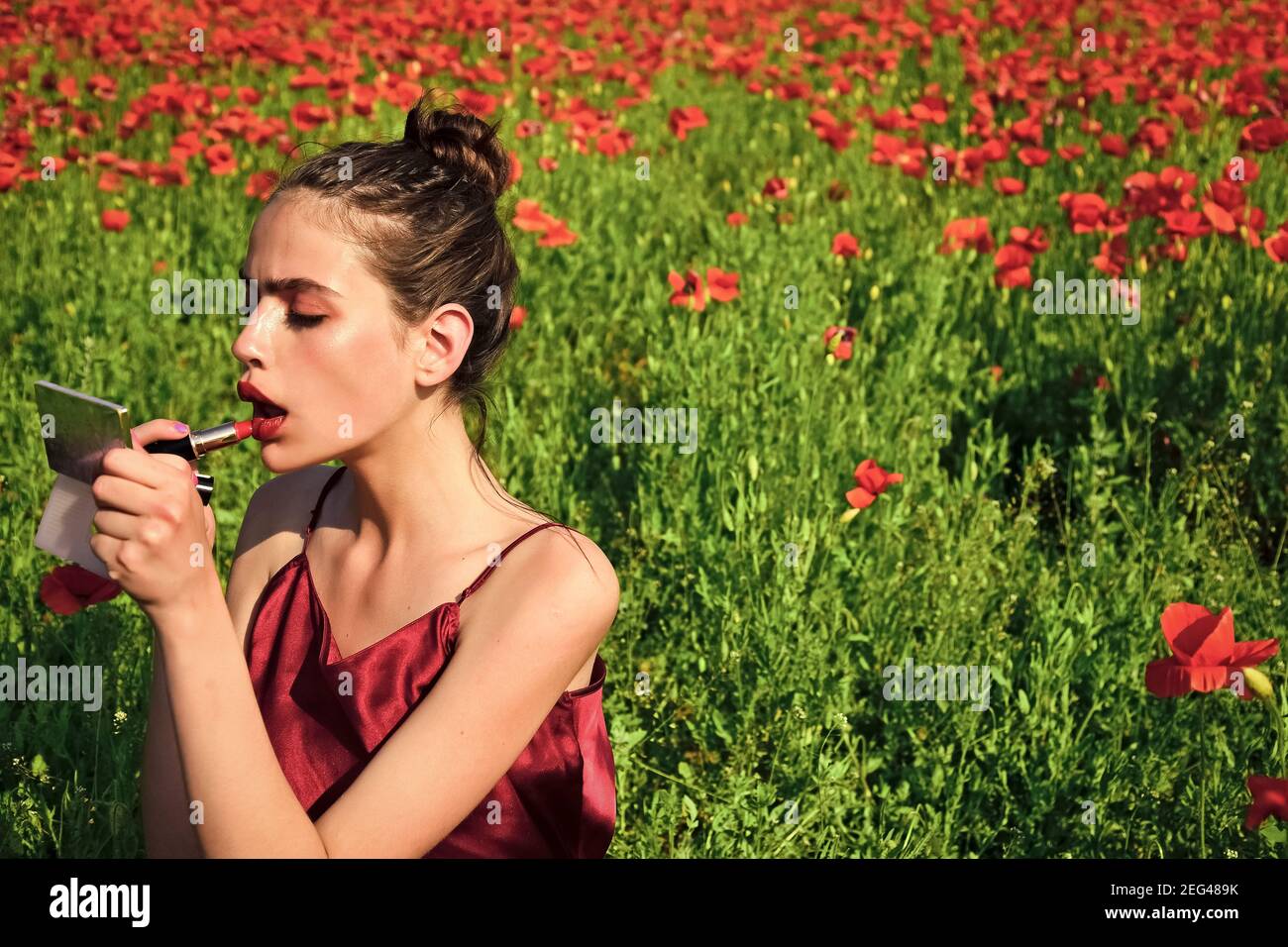Lèvres rouges de jolie femme mettre maquillage avec miroir et rouge à lèvres.  Jeune femme dans le champ de fleurs de pavot, la jeunesse et la fraîcheur  Photo Stock - Alamy