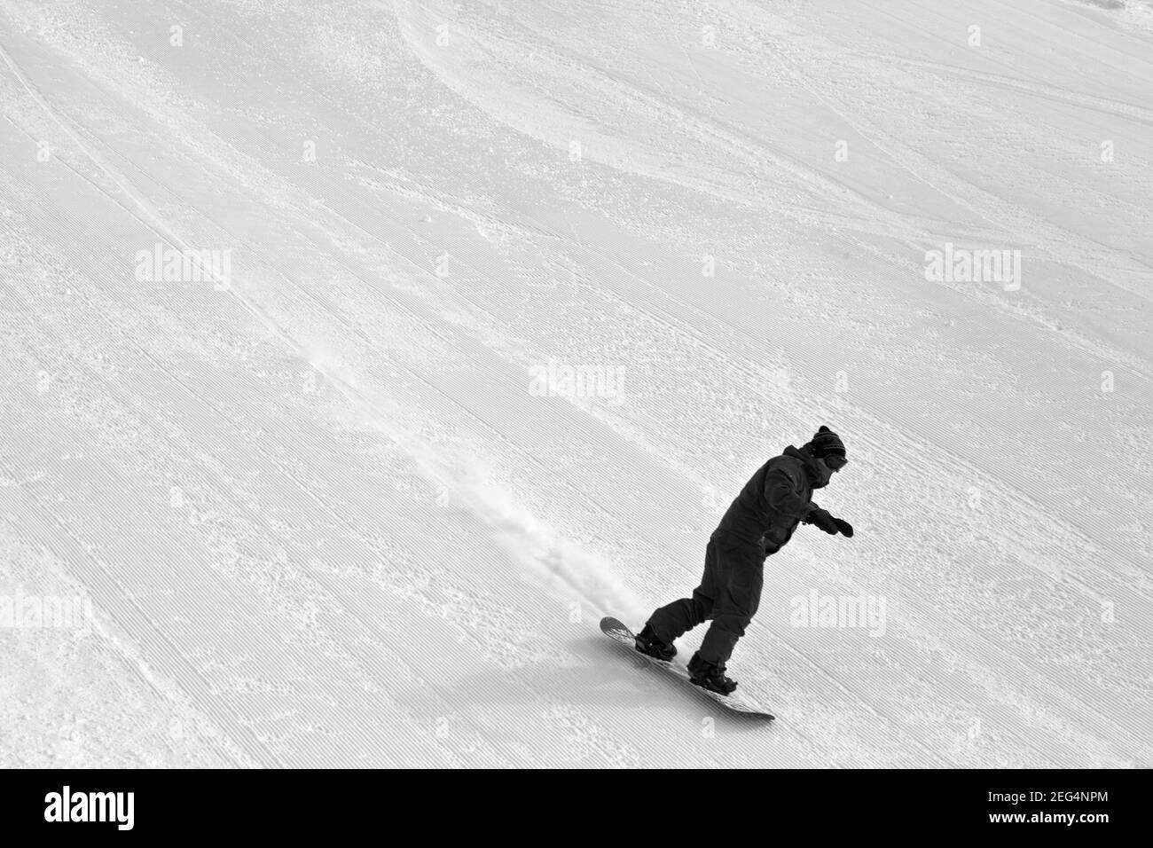 Descente de snowboarders sur une piste de ski pour le toilettage de la neige par temps froid d'hiver. Image en noir et blanc. Banque D'Images