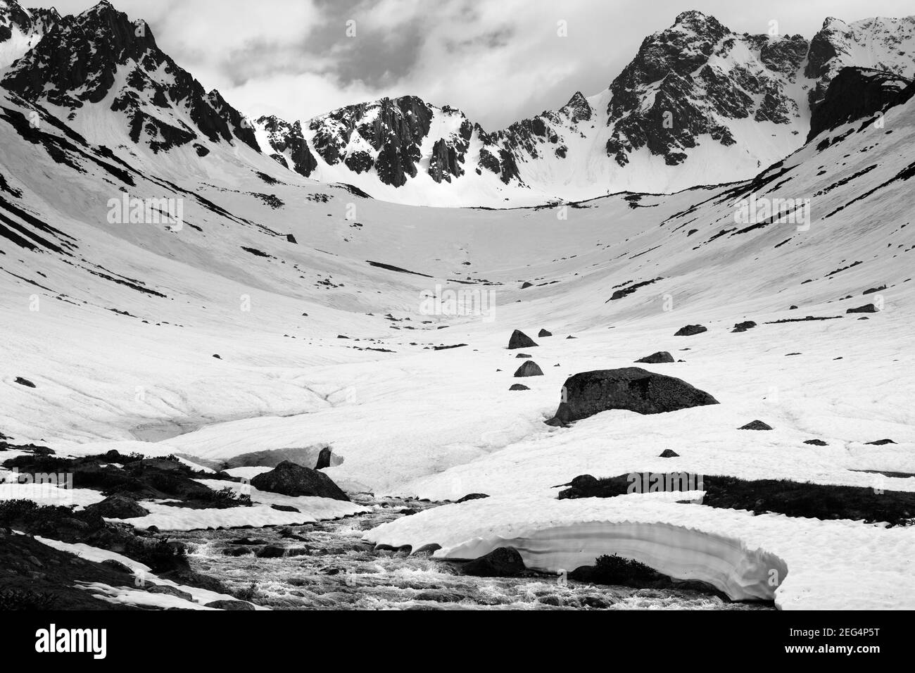 Rivière avec ponts de neige dans les hautes montagnes enneigées au printemps soir. Turquie, montagnes Kachkar, partie la plus haute des montagnes Pontiques. Tons noir et blanc Banque D'Images