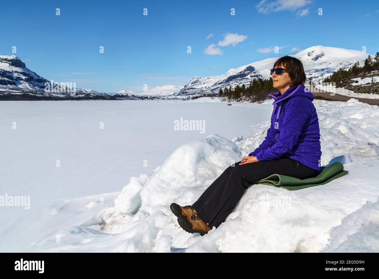 Femme assise dans une dérive des neiges et profitant du soleil au printemps, Stora sjöfallets nationalpark, patrimoine mondial de Laponia, Laponie suédoise, Suède Banque D'Images