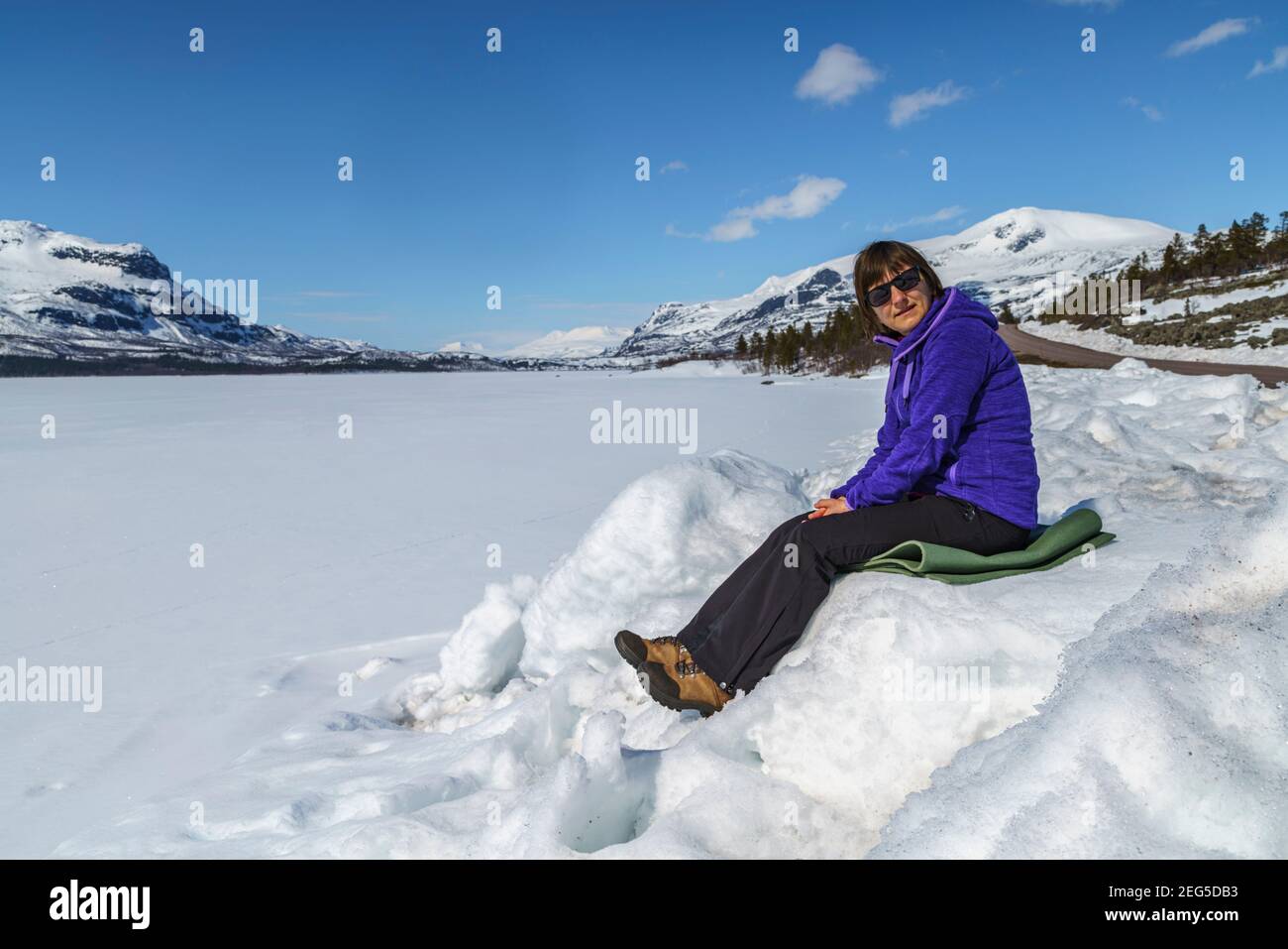 Femme assise dans une dérive des neiges et profitant du soleil au printemps, Stora sjöfallets nationalpark, patrimoine mondial de Laponia, Laponie suédoise, Suède Banque D'Images