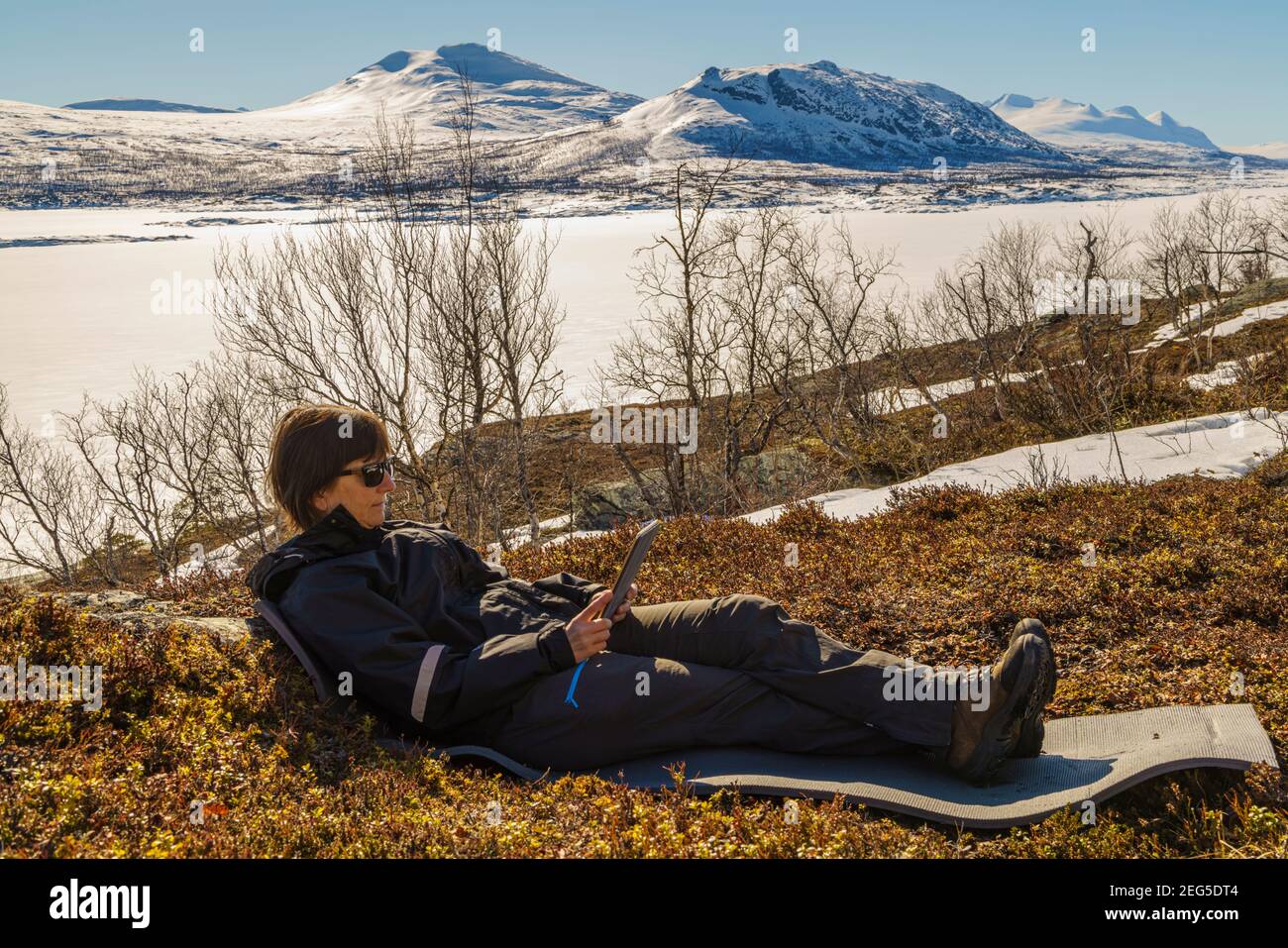Femme couchée en montagne à l'aide de son tableau, au parc national Stora sjöfallets au printemps avec de la neige autour et sur les montagnes, S Banque D'Images