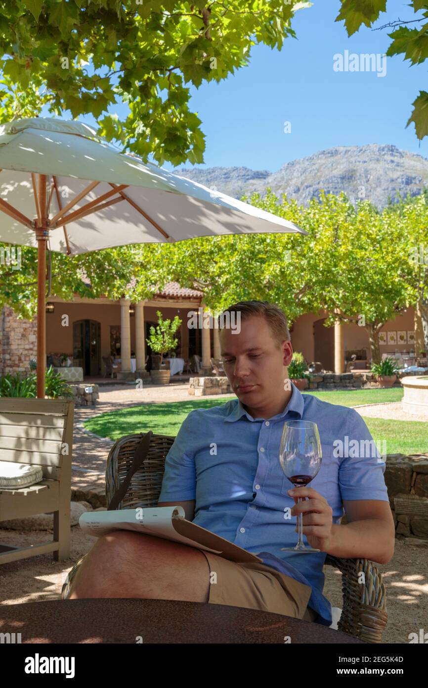 Homme blanc assis avec un verre de vin dans sa main lisant le menu, domaine viticole de Waterford, Stellenbosch, Afrique du Sud Banque D'Images