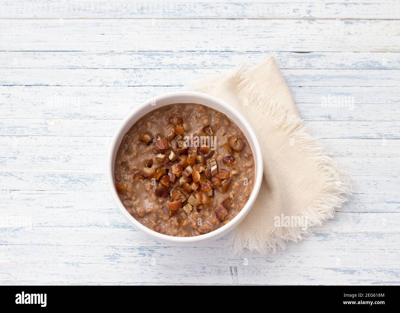 Délicieux flocons d'avoine dans un bol blanc, dattes fruits et cacao. Petit déjeuner sain sur fond bleu clair. Vue du dessus Banque D'Images