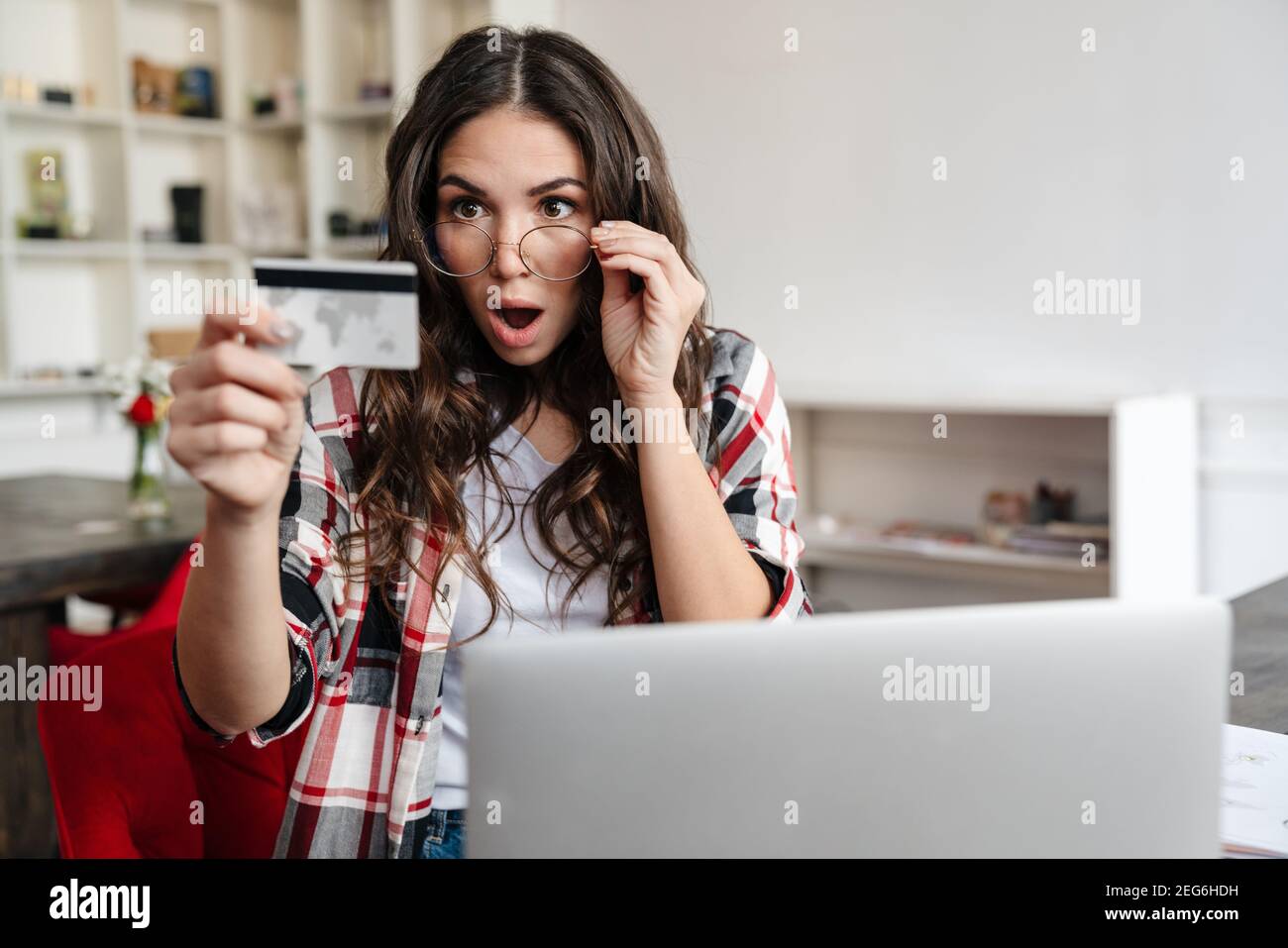 Choqué brune femme tenant la carte de crédit tout en travaillant avec un ordinateur portable dans le café Banque D'Images