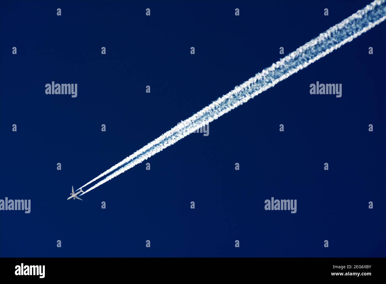 Avion à haute altitude volant à travers un ciel bleu clair laissant des traînées de vapeur dans la lumière du soleil en fin d'après-midi Banque D'Images
