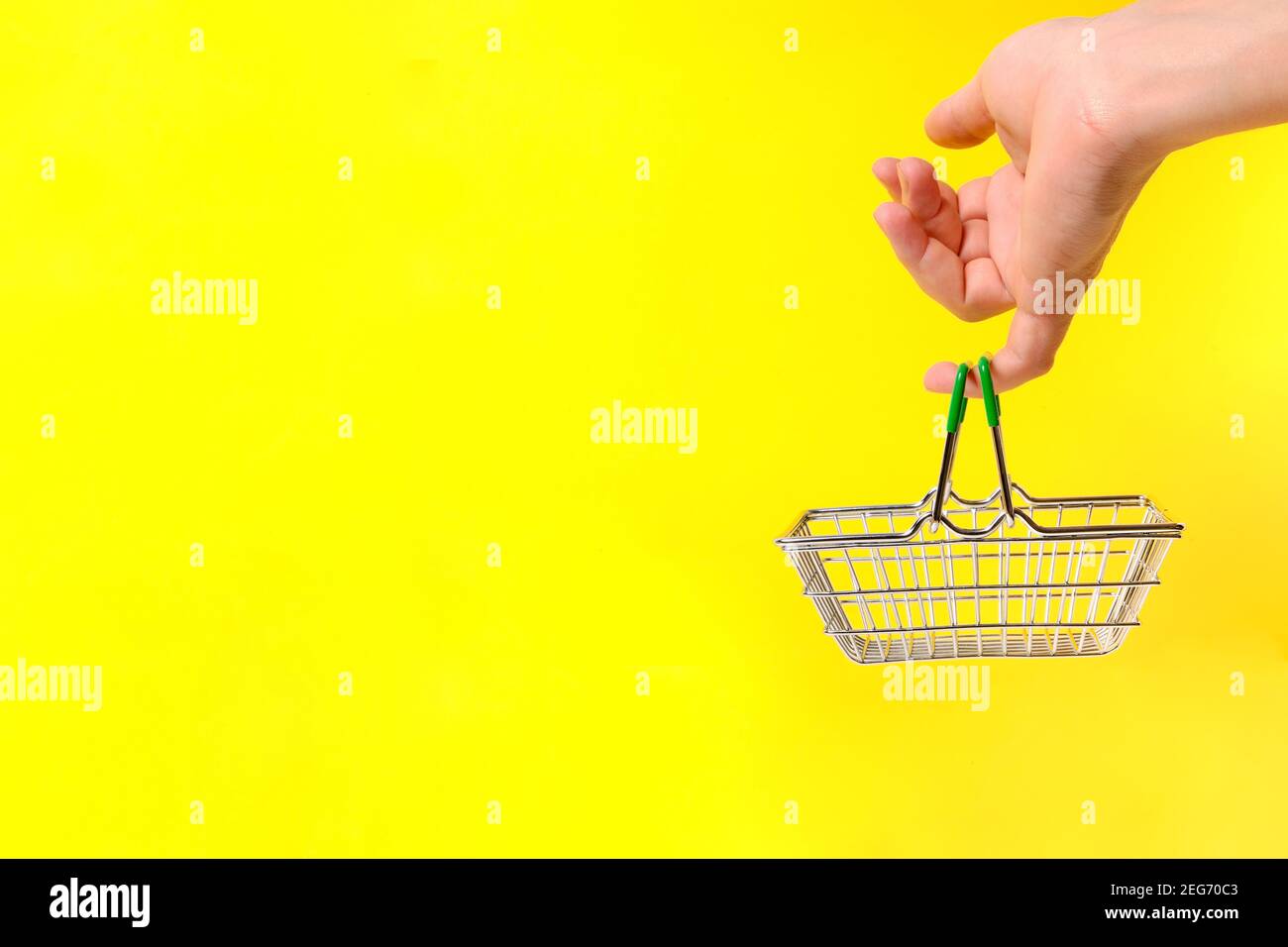 Main tient le panier avec son petit doigt, sur fond jaune. Concept d'un voyage au supermarché. Banque D'Images