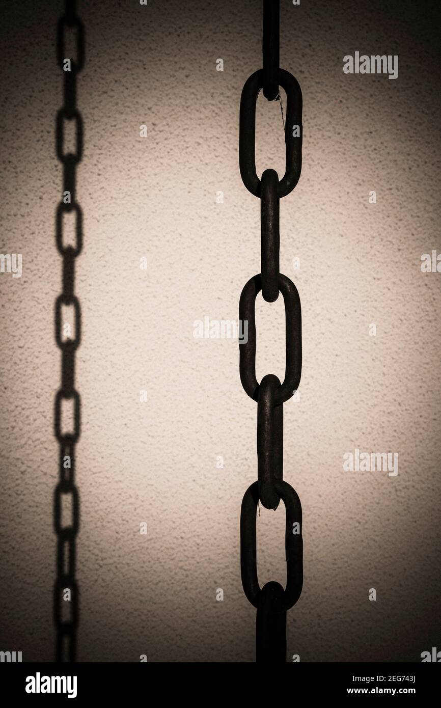 Les chaînes en métal noir suspendues sur un fond texturé créent un contraste visuel saisissant dans un espace sombre Banque D'Images