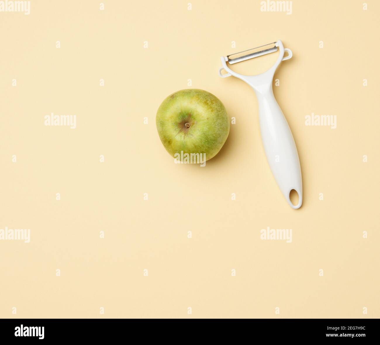 tenant un couteau en plastique pour nettoyer les légumes, les fruits et une pomme verte sur un fond beige, vue du dessus Banque D'Images