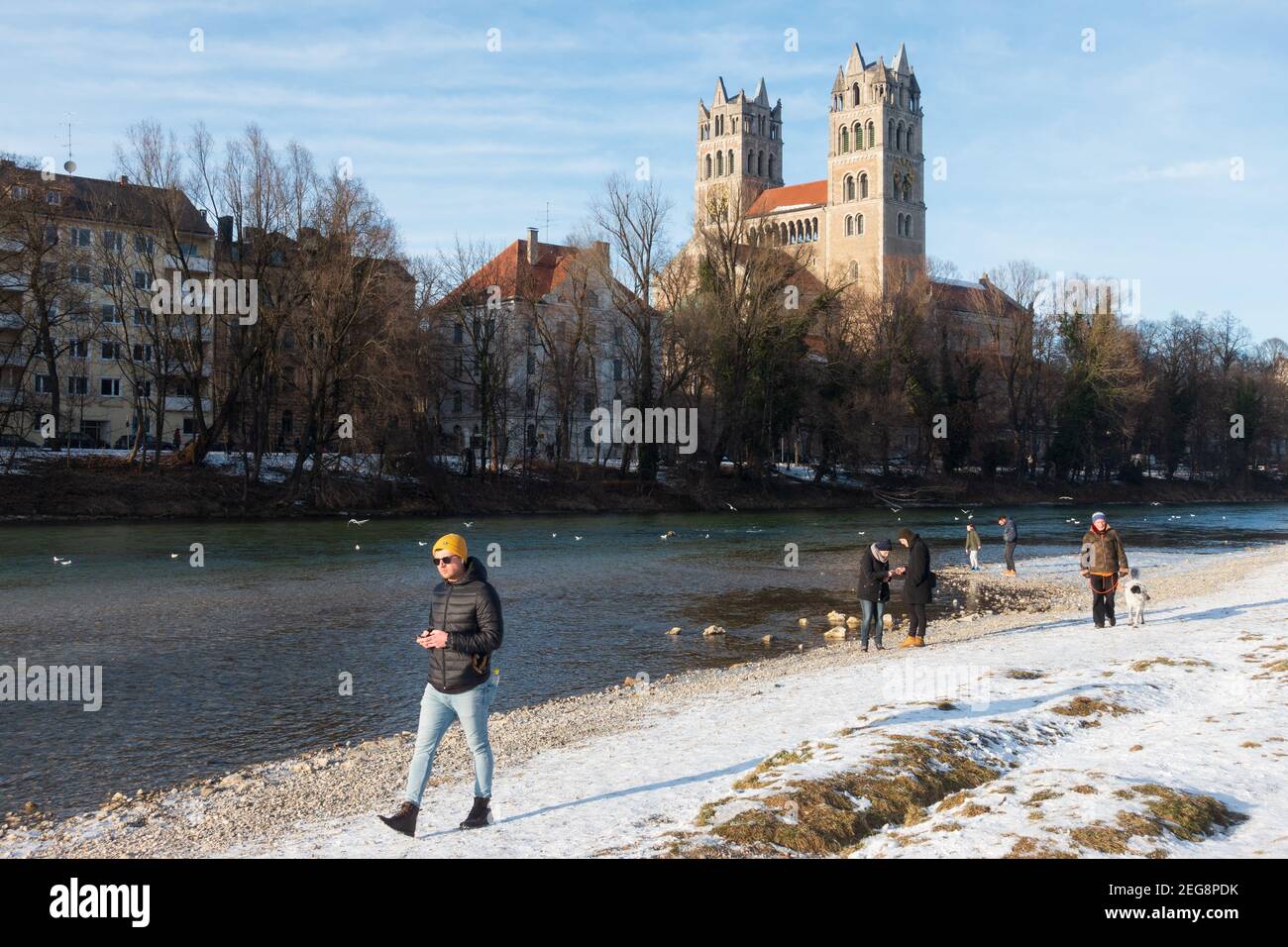 Munich, Allemagne - 13 février 2021 : l'homme marche avec son téléphone portable à côté de l'église St Maximilian depuis le front d'eau de l'Isar. Les gens qui marchent le long Banque D'Images