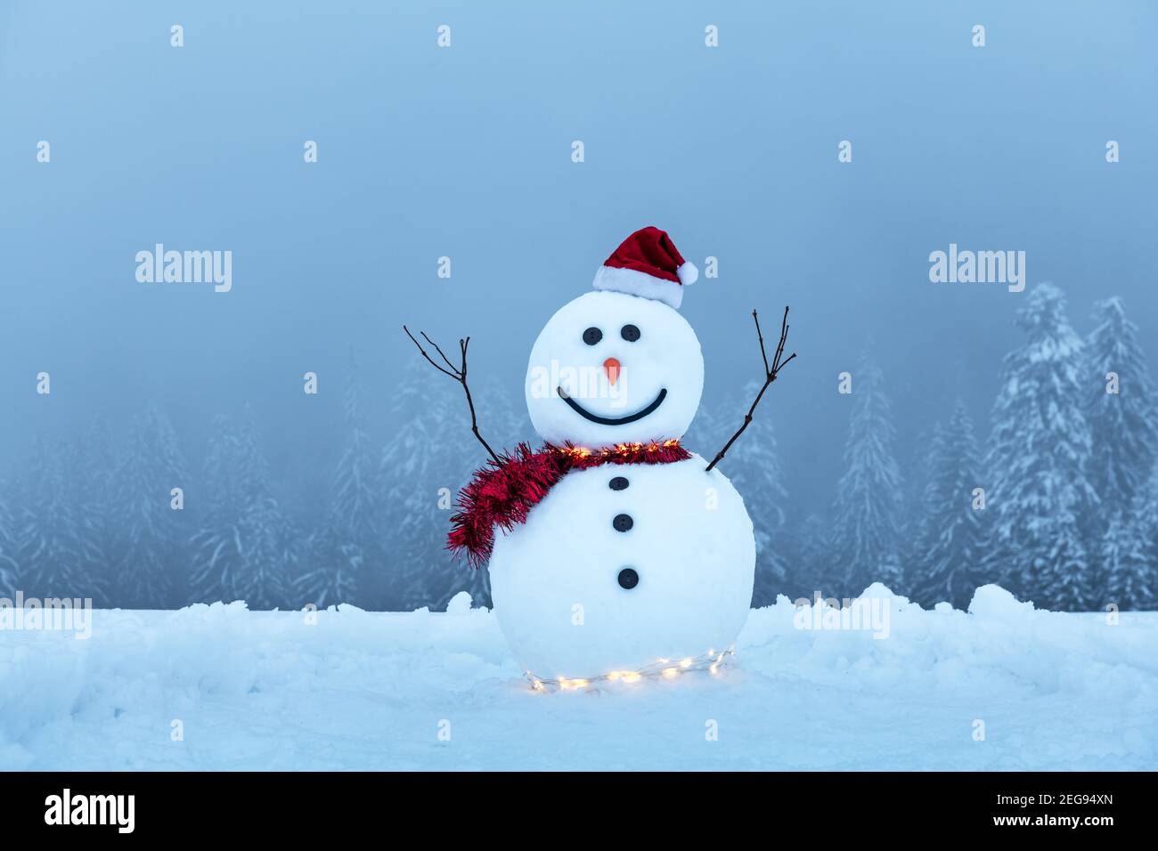 Bonhomme de neige amusant dans un élégant chapeau rouge et un rouge éboulé sur des montagnes enneigées. Guirlande lumineuse pour les fêtes de Noël Banque D'Images