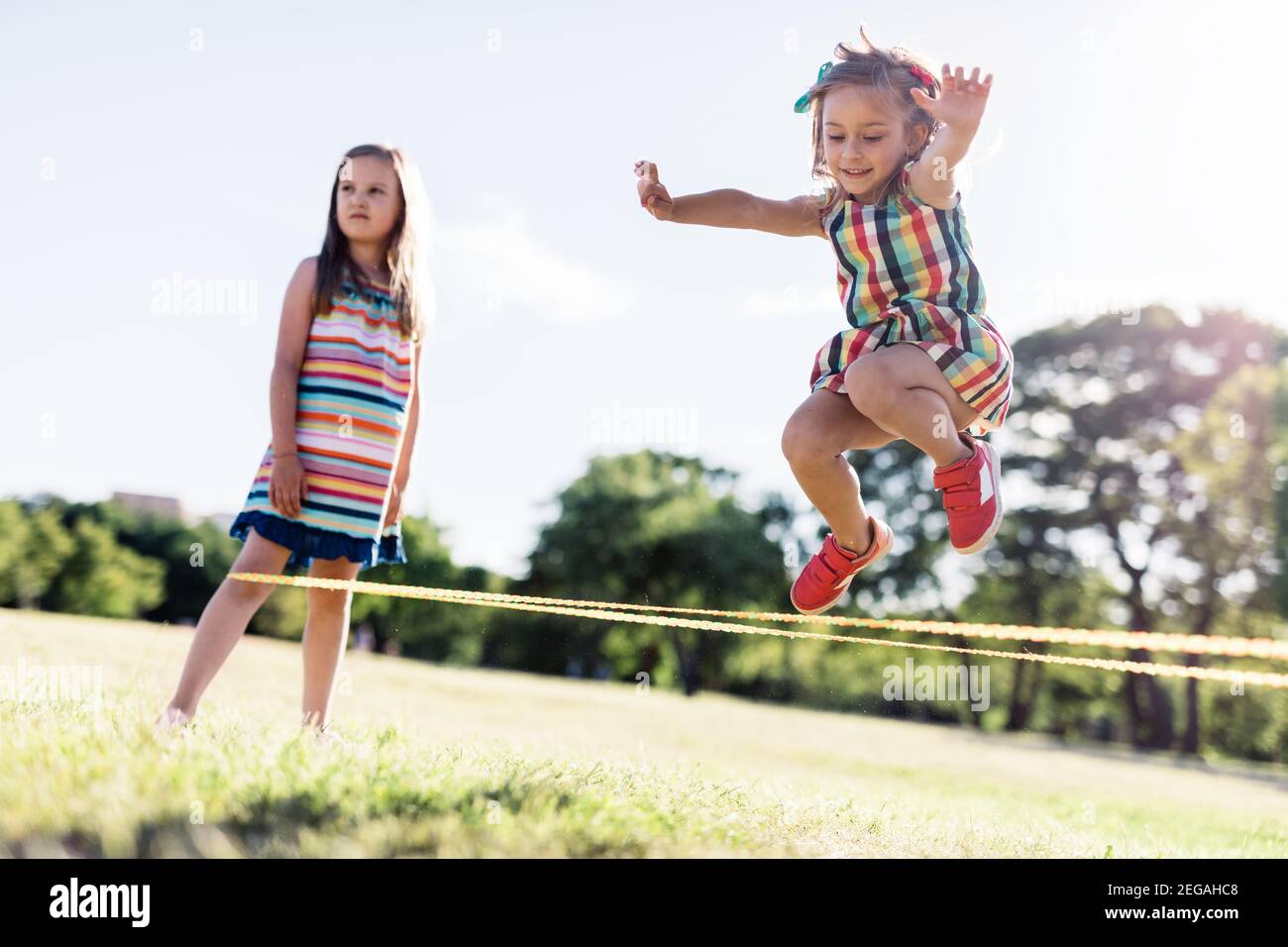 Petite fille dans une robe colorée sautant à travers l'élastique. Jeu  d'enfance. Corde à sauter chinoise Photo Stock - Alamy