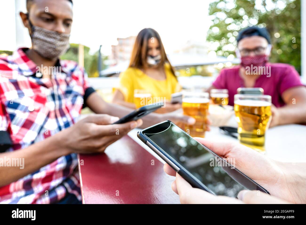 Ennuient des amis avec des masques médicaux à l'aide de l'application de traçage avec Smartphones mobiles - Nouveau concept de style de vie normal par les jeunes à la barre d'air ouverte Banque D'Images