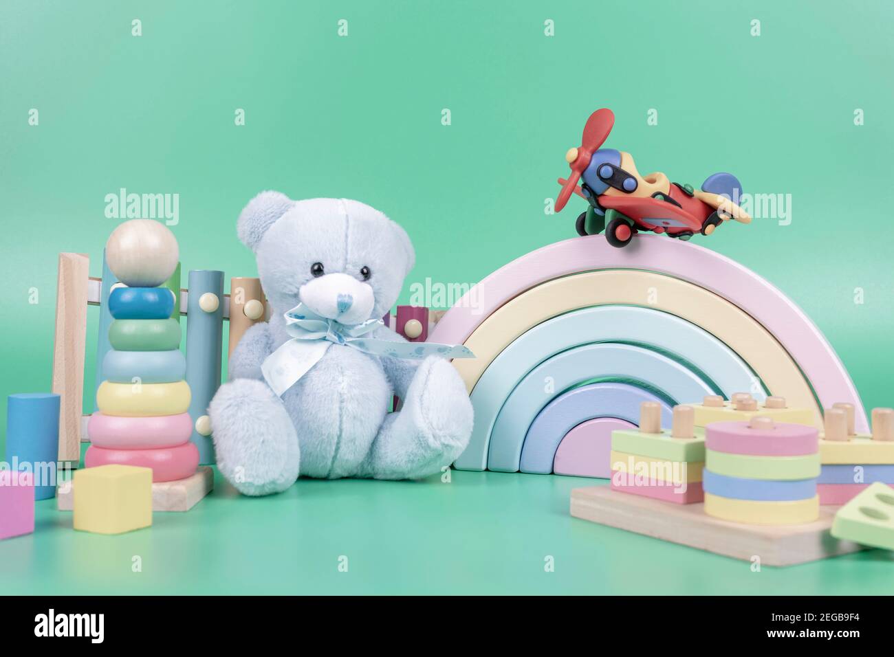 Collection de jouets pour enfants. Ours en peluche, arc-en-ciel en bois, avions, jouets éducatifs et musicaux pour bébés sur fond vert clair Banque D'Images