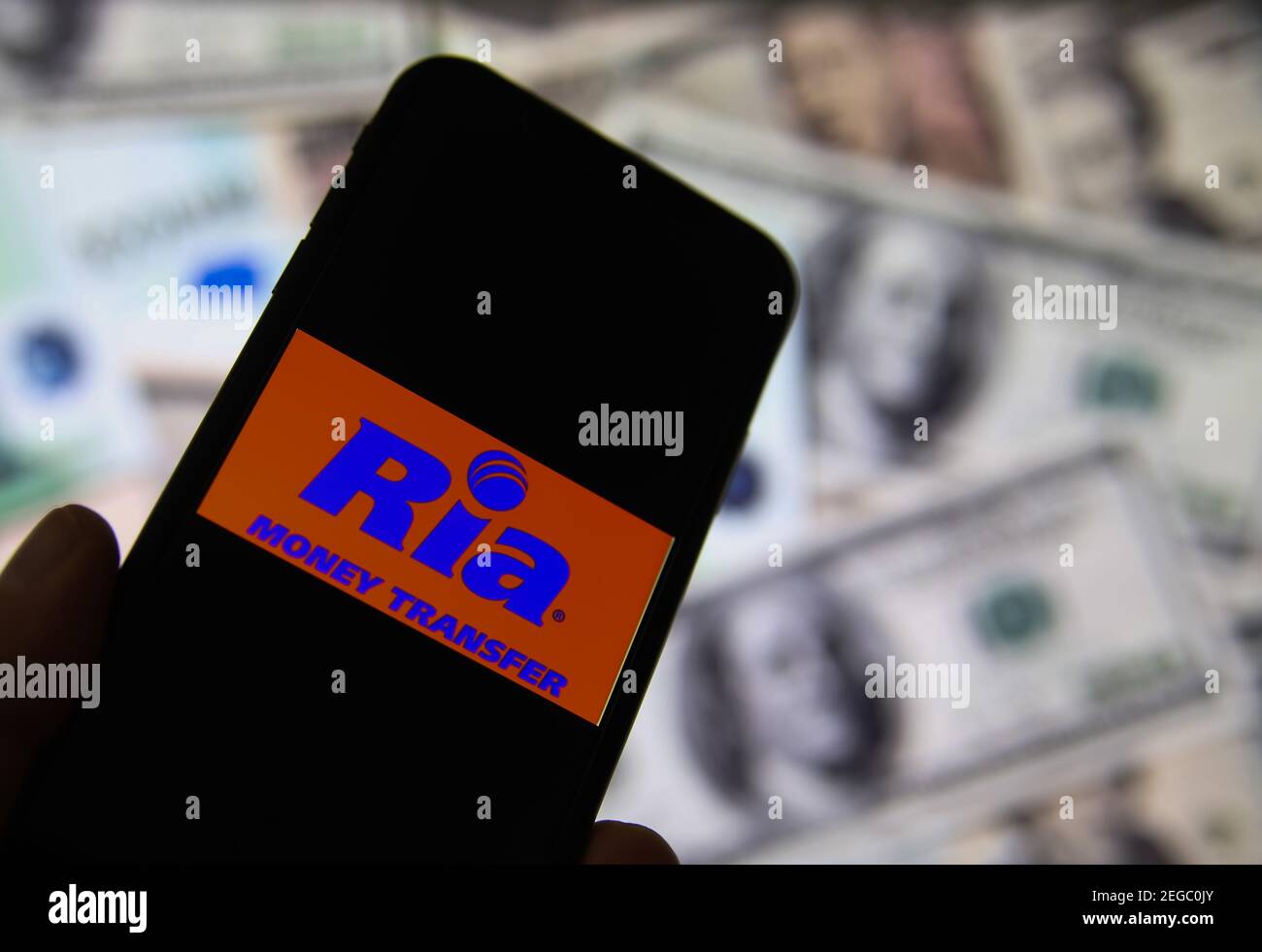 Viersen, Allemagne - février 9. 2020: Gros plan de l'écran de smartphone avec logo lettrage du service de transfert d'argent en ligne ria, billets flous backgrou Banque D'Images