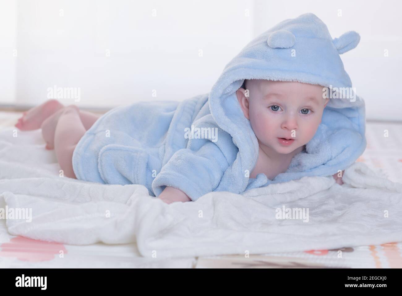 Mignon heureux rire bébé garçon dans un peignoir doux après le bain jouant  sur le lit blanc avec des oreillers bleus et roses dans la chambre  ensoleillée des enfants. Enfant dans propre
