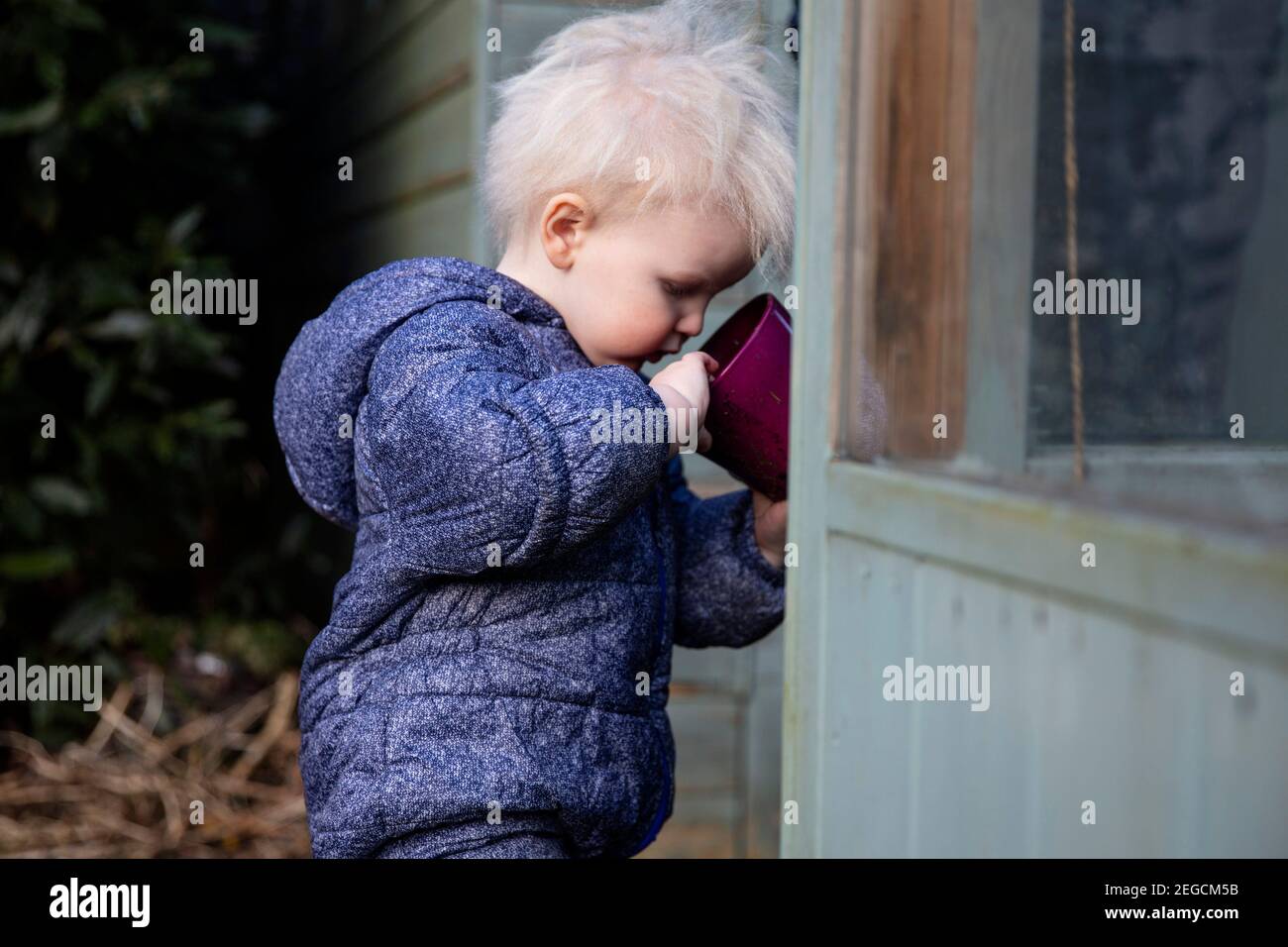 Mignon jeune garçon jouant dans le jardin avec un pot de fleurs Banque D'Images