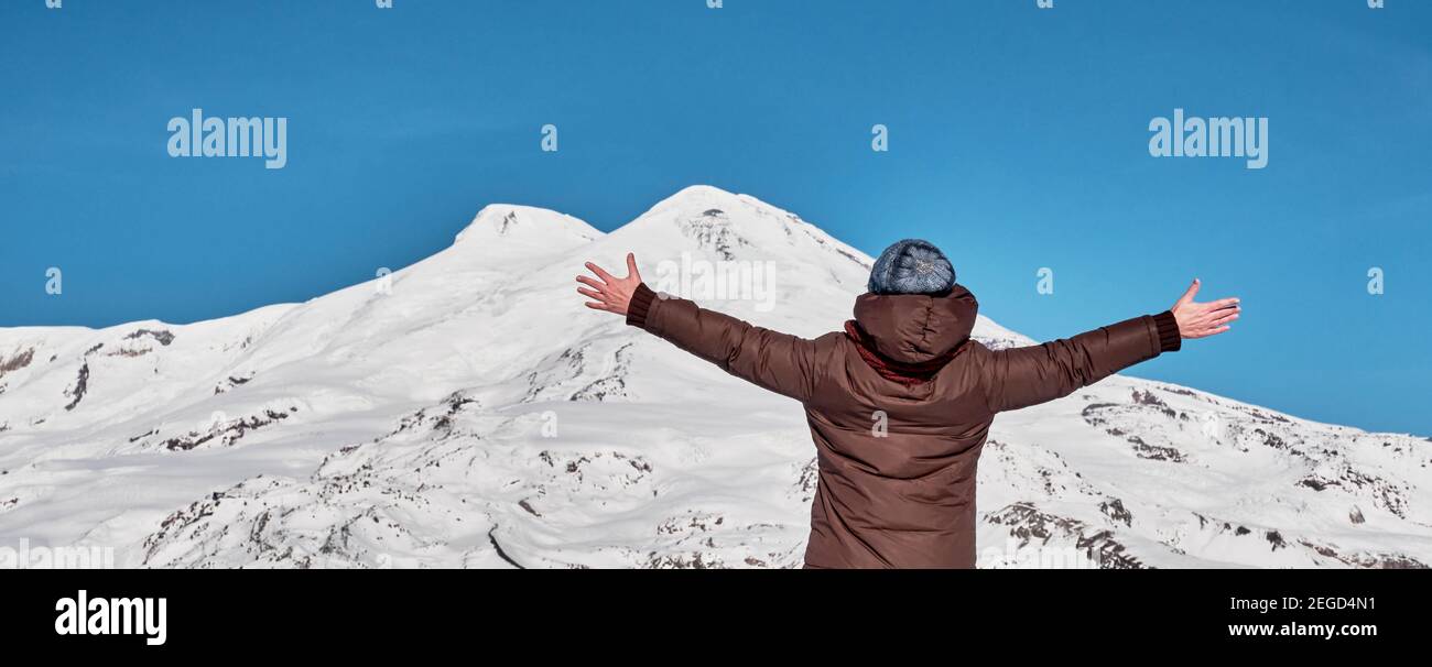 Paysage de montagne d'hiver. Une femme en veste chaude et un bonnet tricoté  lui a levé les mains en saluant sur le fond de deux sommets du mont Elbrus  Photo Stock -