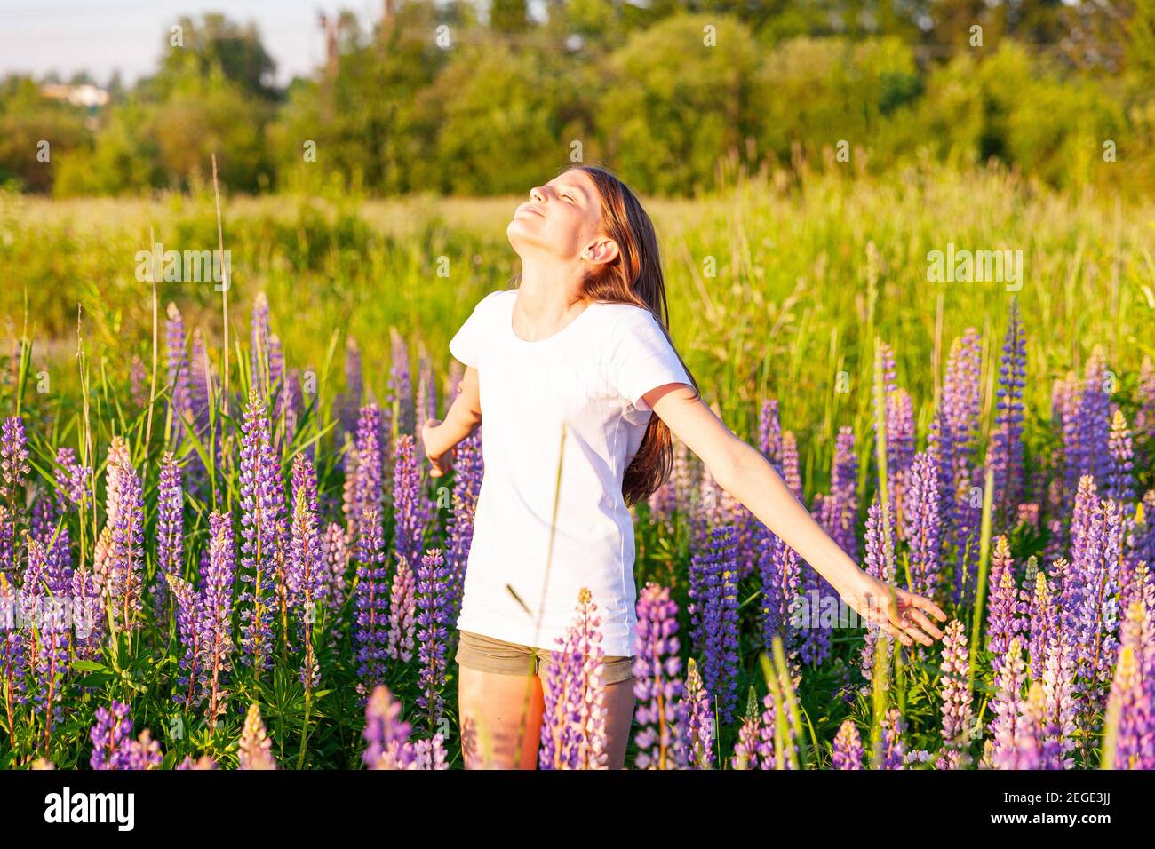 Bonne adolescente souriante à l'extérieur. Belle jeune femme de l'adolescence se reposant sur le terrain d'été avec fleurs sauvages fleur de fond vert. T-shirt enfant gratuit Banque D'Images
