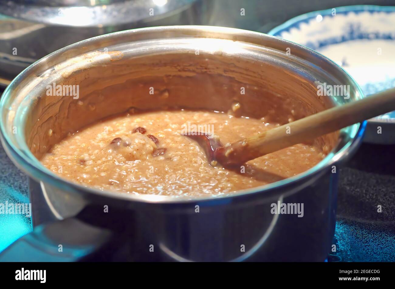 Céréales pour le petit déjeuner saines. Avoine coupée en acier avec raisins secs et un soupçon de cuisson à la cannelle dans une casserole en acier inoxydable avec une cuillère en bois. Banque D'Images